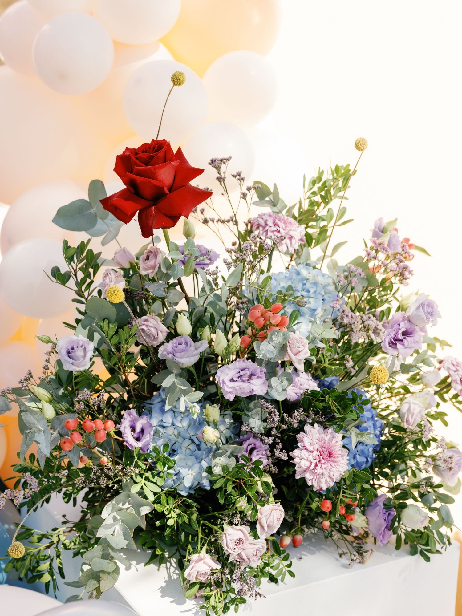 Elegant floral arrangement featuring red roses, purple blooms, and eucalyptus in a modern asymmetrical design.