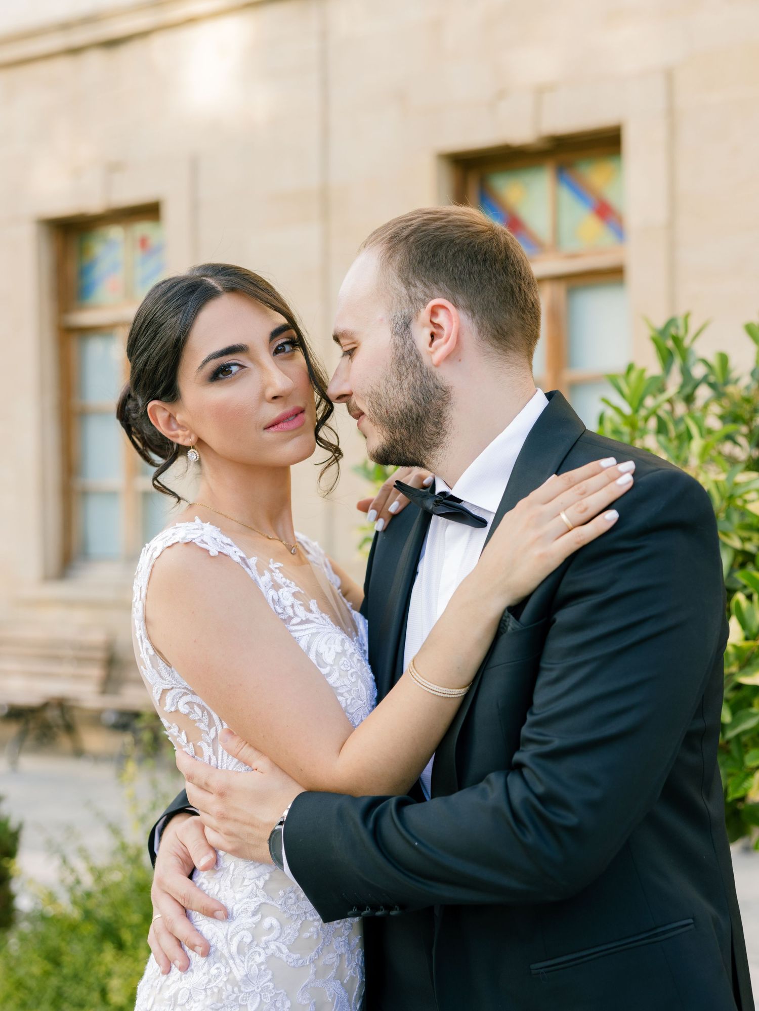 Tender moment between newlyweds against stone wall with greenery.