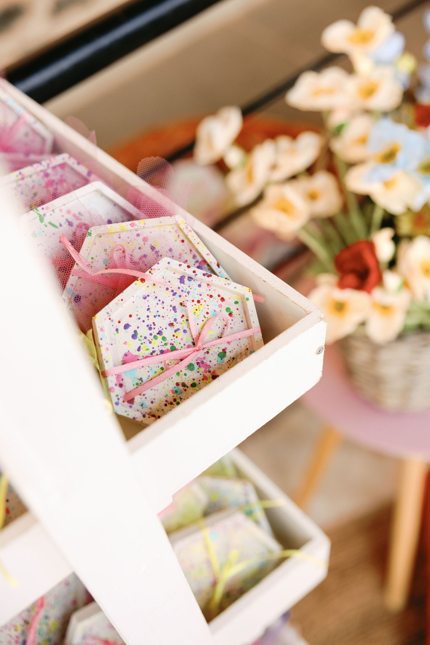 A close-up view of pink frosted desserts with colorful sprinkles in white boxes alongside delicate white flowers.