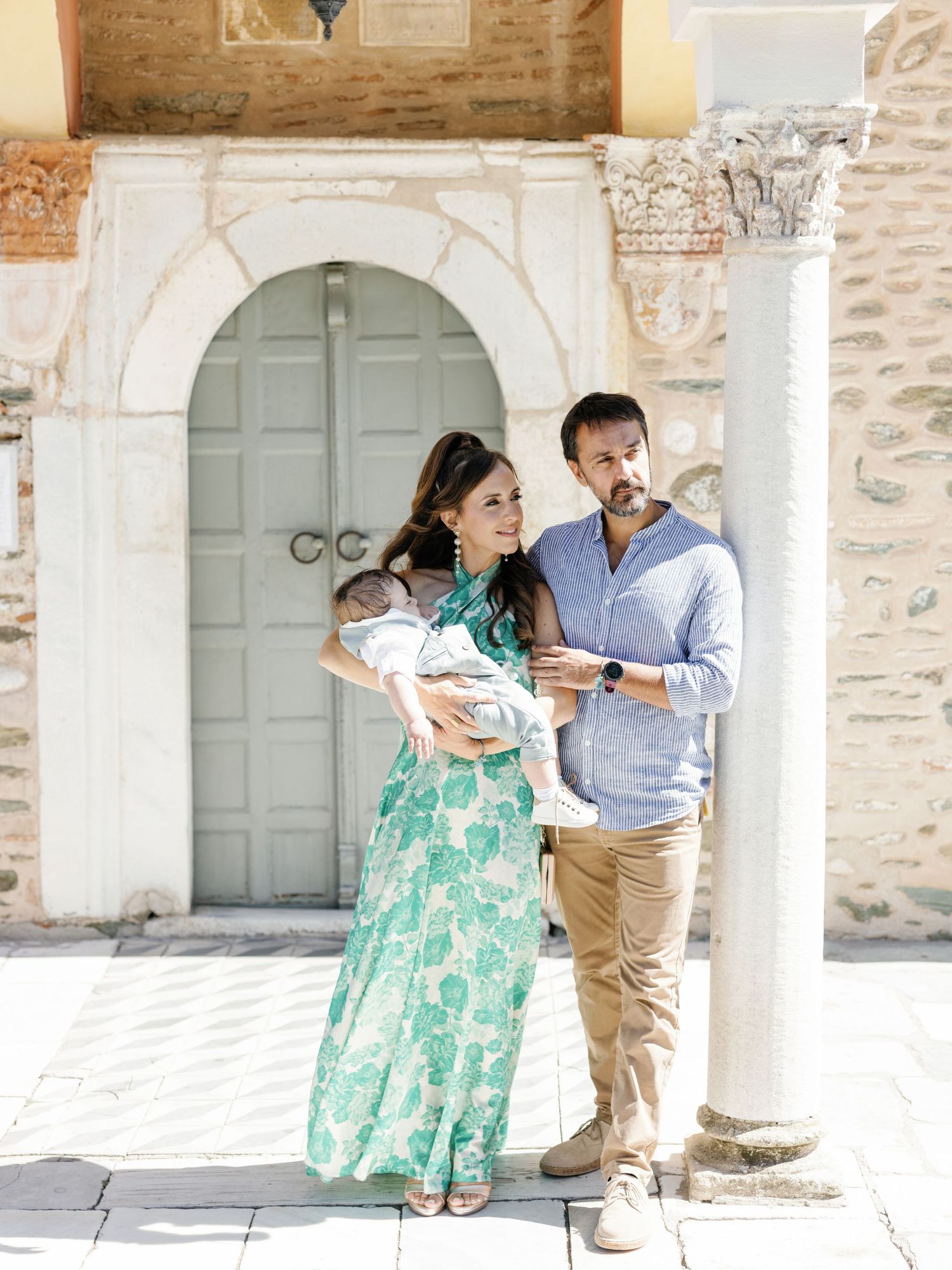 A parent and child in matching green floral dresses share a tender moment against a rustic stone wall backdrop.