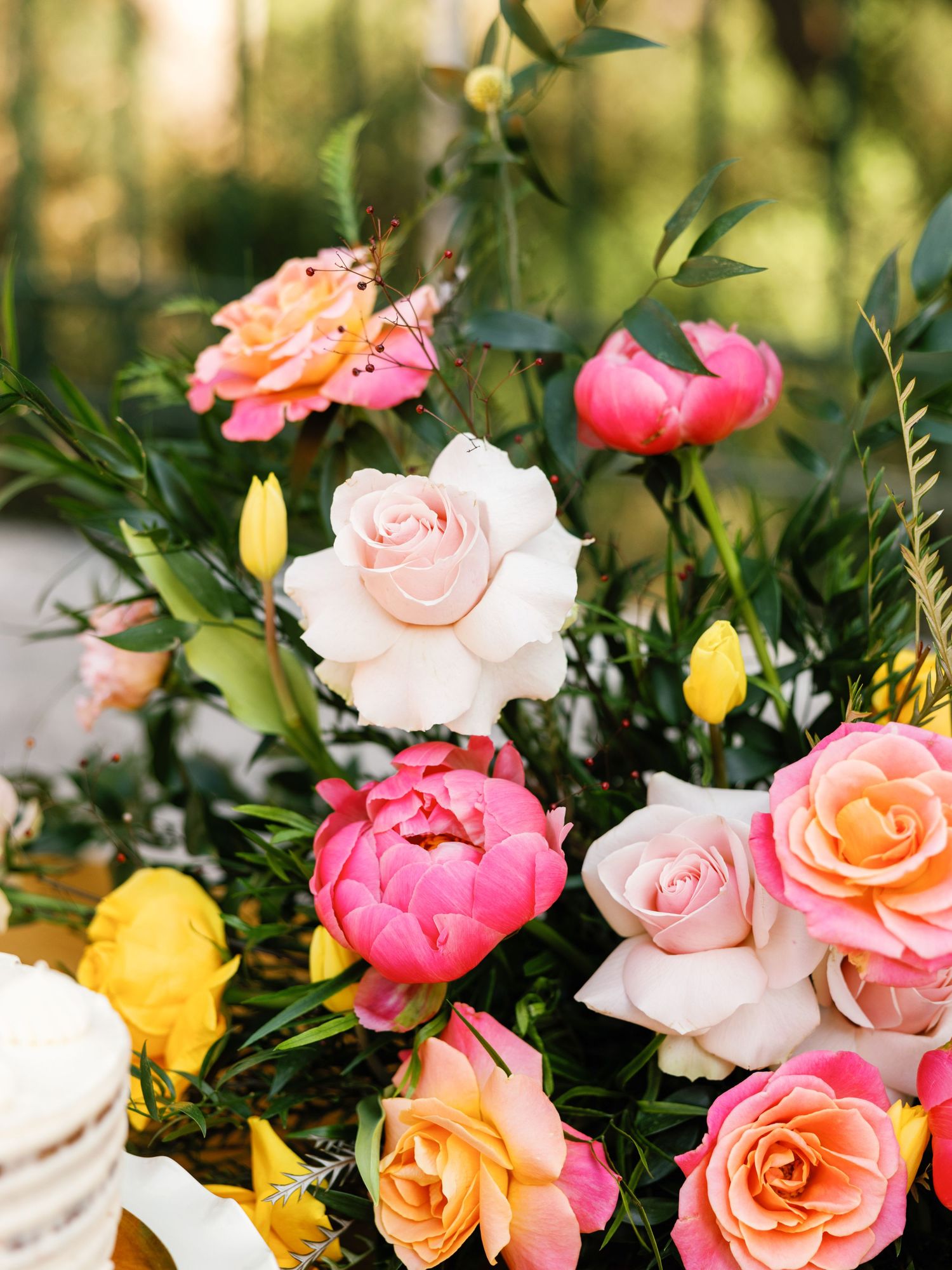 A lush garden arrangement of pink, peach, and yellow roses with green foliage in natural outdoor lighting.