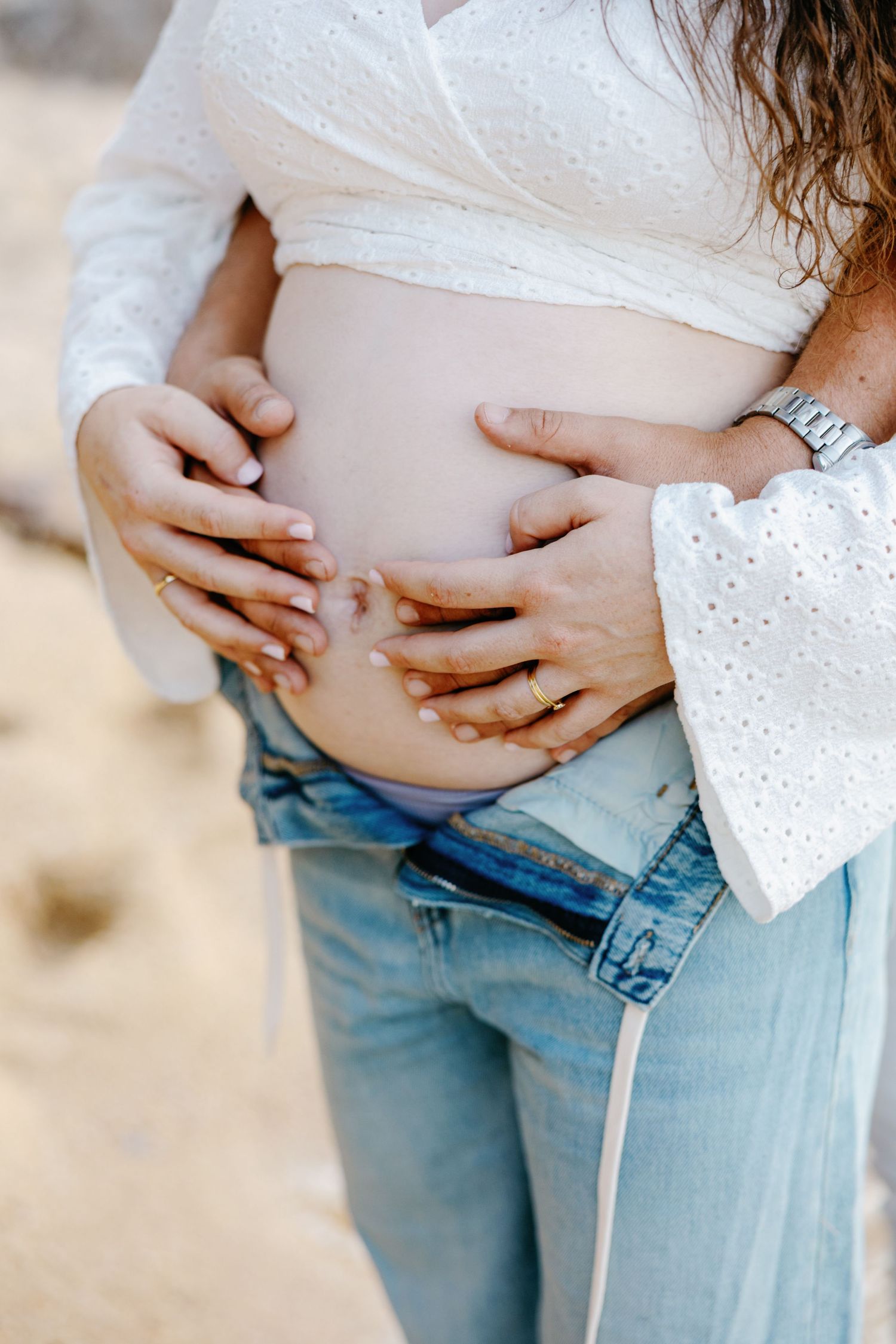 Close-up shots of hands cradling a pregnant belly in white eyelet top and jeans.