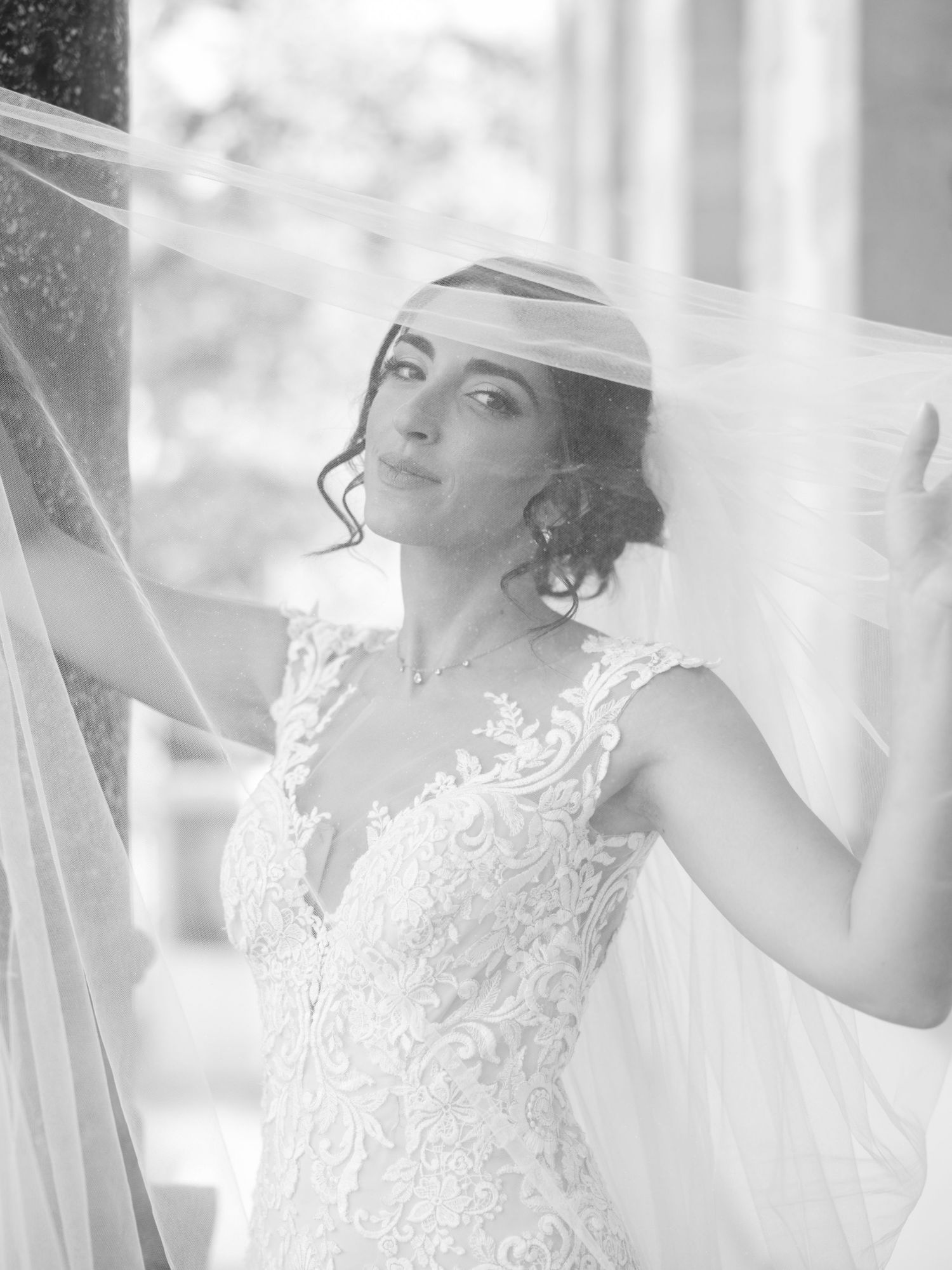 Dreamy black and white bridal portrait with flowing veil against architectural backdrop.
