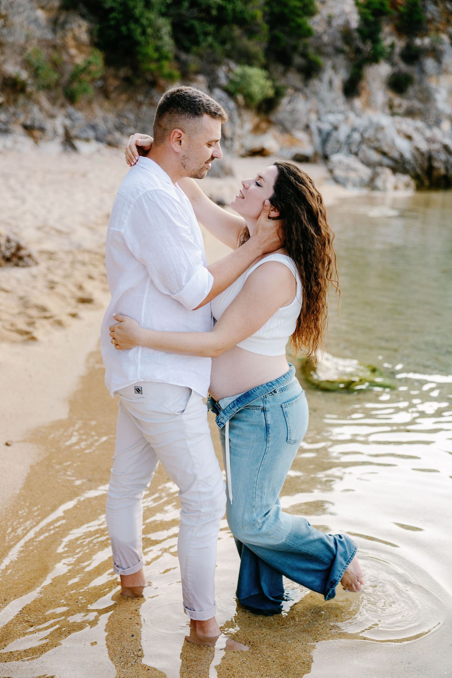 A couple plays in shallow water during a romantic beach photoshoot.