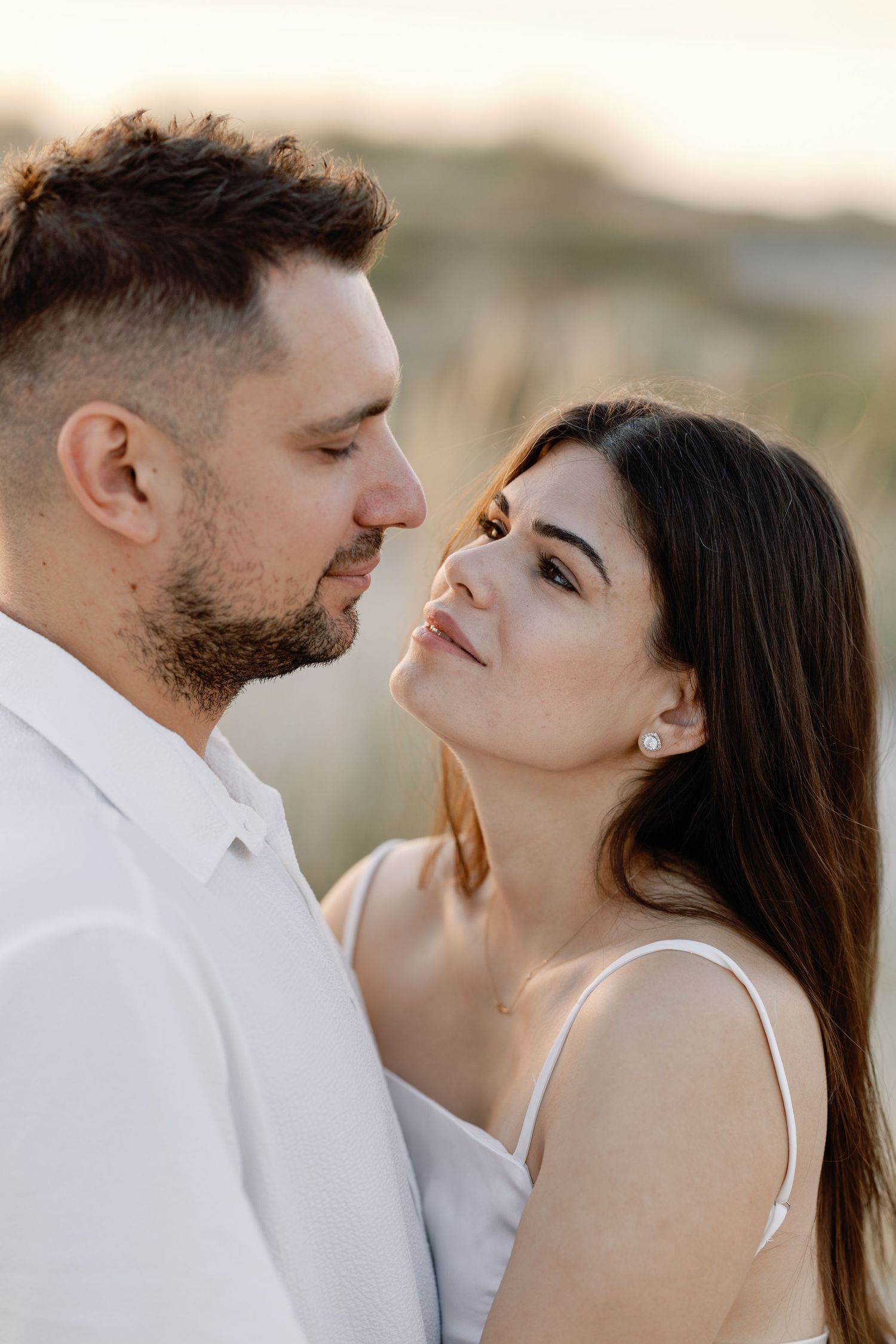 Romantic couple sharing intimate moments in white outfits against a soft natural backdrop.