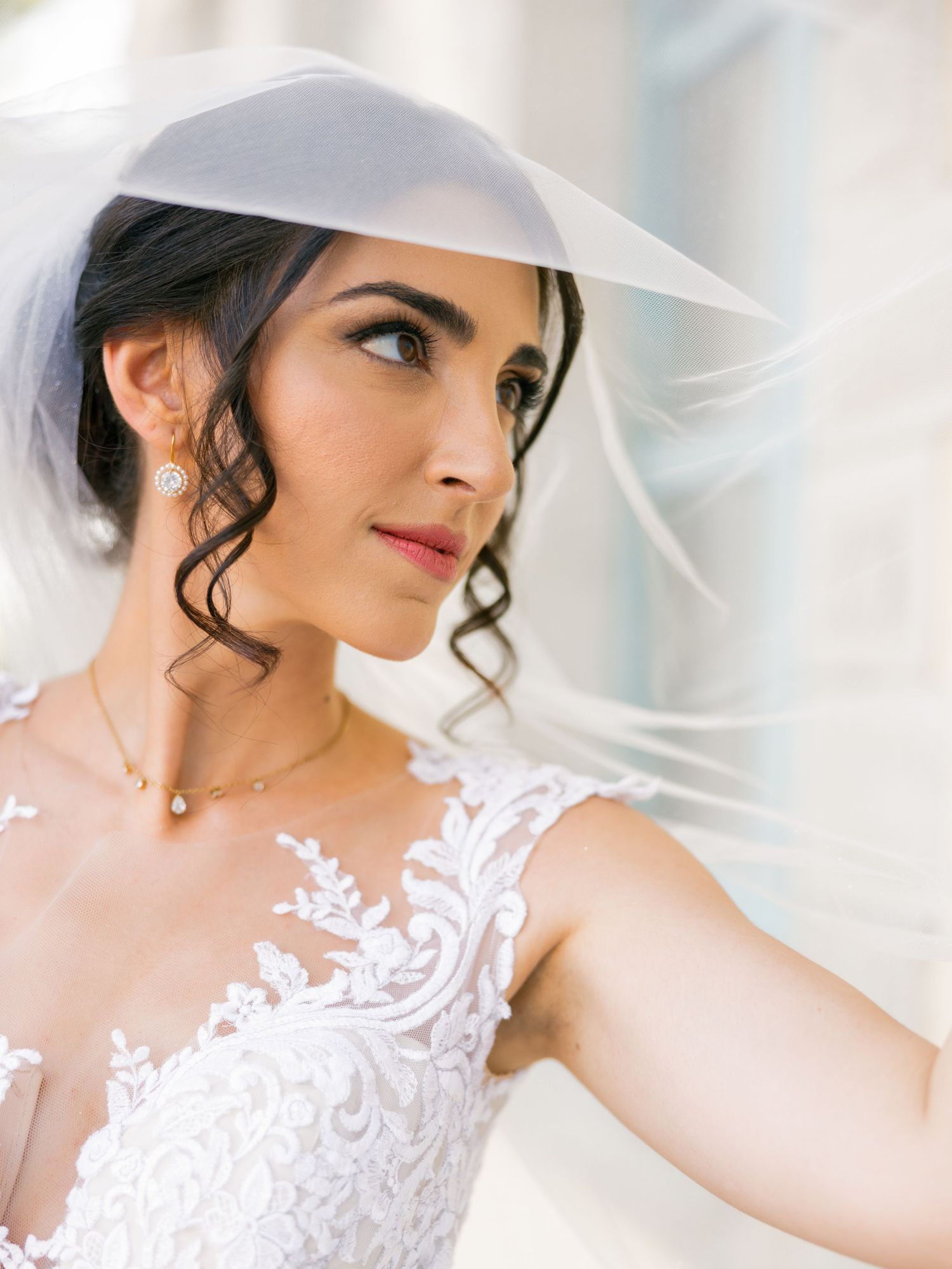 Close up details of delicate white lace wedding dress and veil against soft background.
