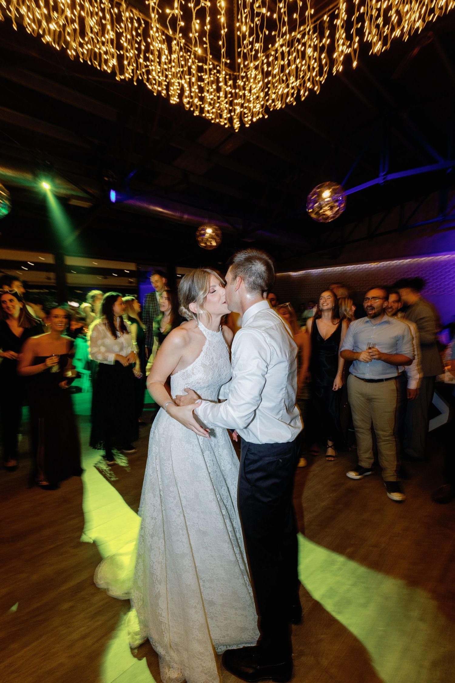 Couples dancing at a wedding reception under colorful lighting and golden decorative ceiling.