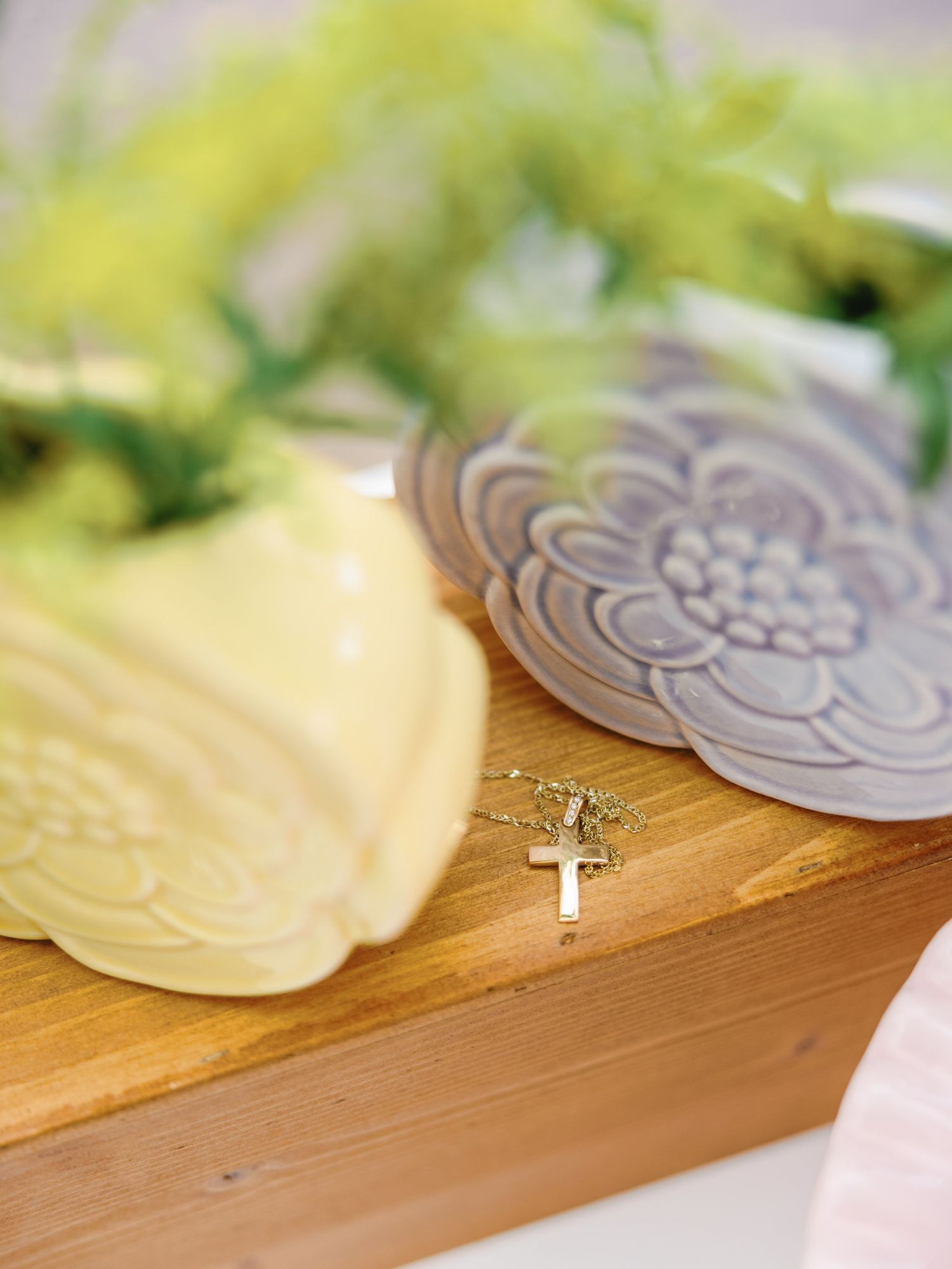 A delicate gold cross necklace pendant rests on a wooden surface beside floral-patterned coasters.