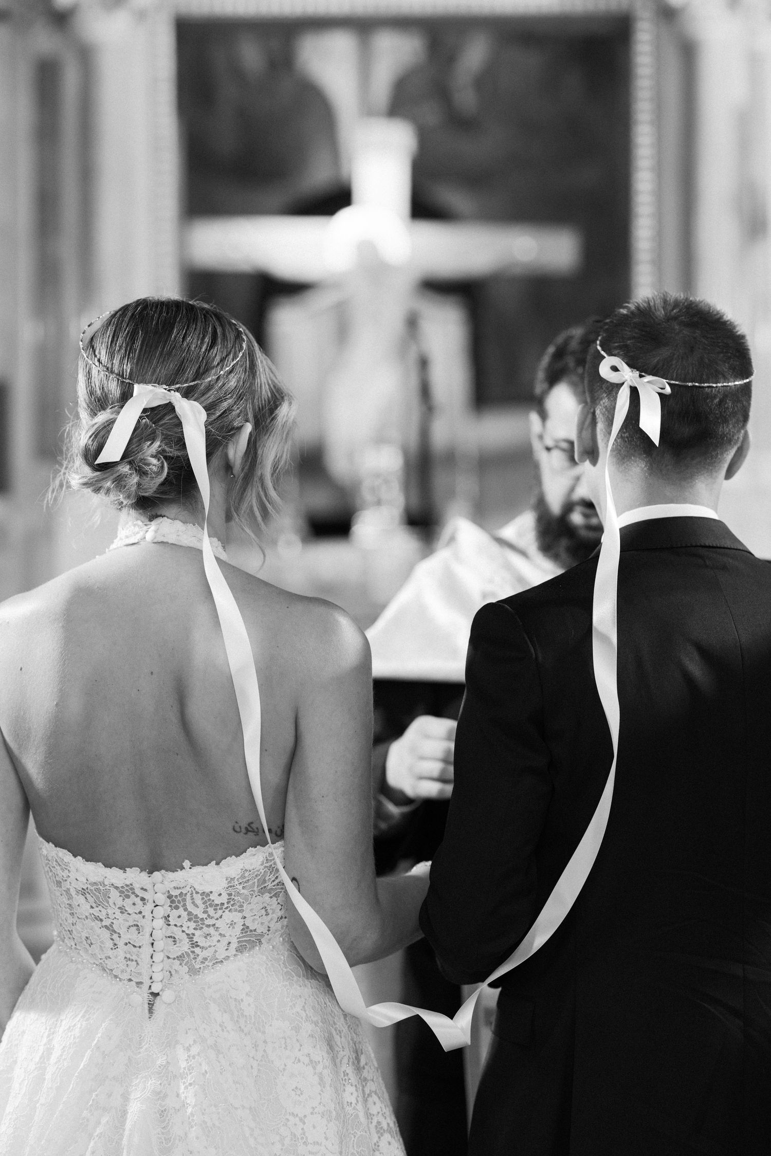 Back view of wedding ceremony attendees standing in formal attire with white dress details visible.