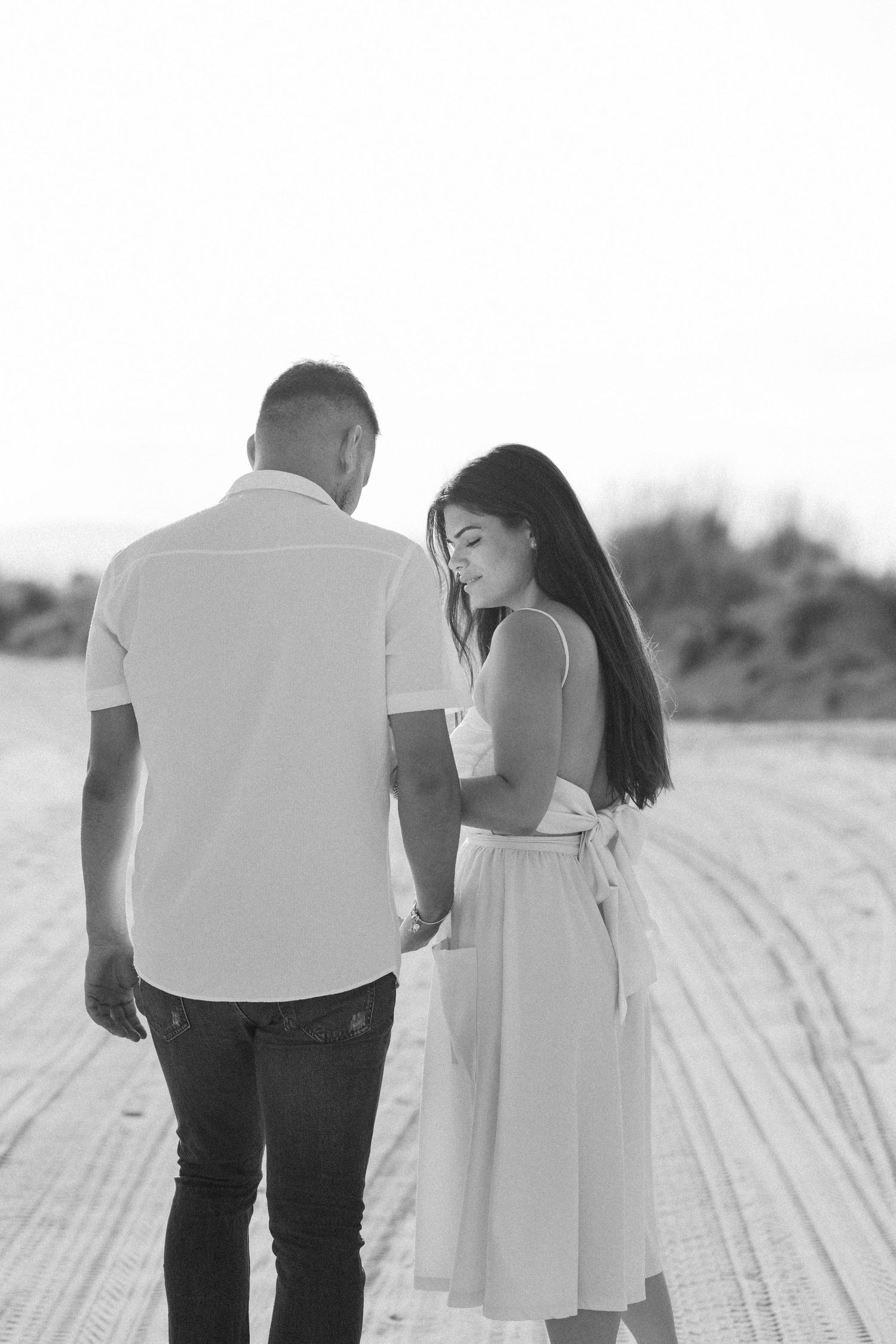Black and white images of couple walking together on textured sandy path.