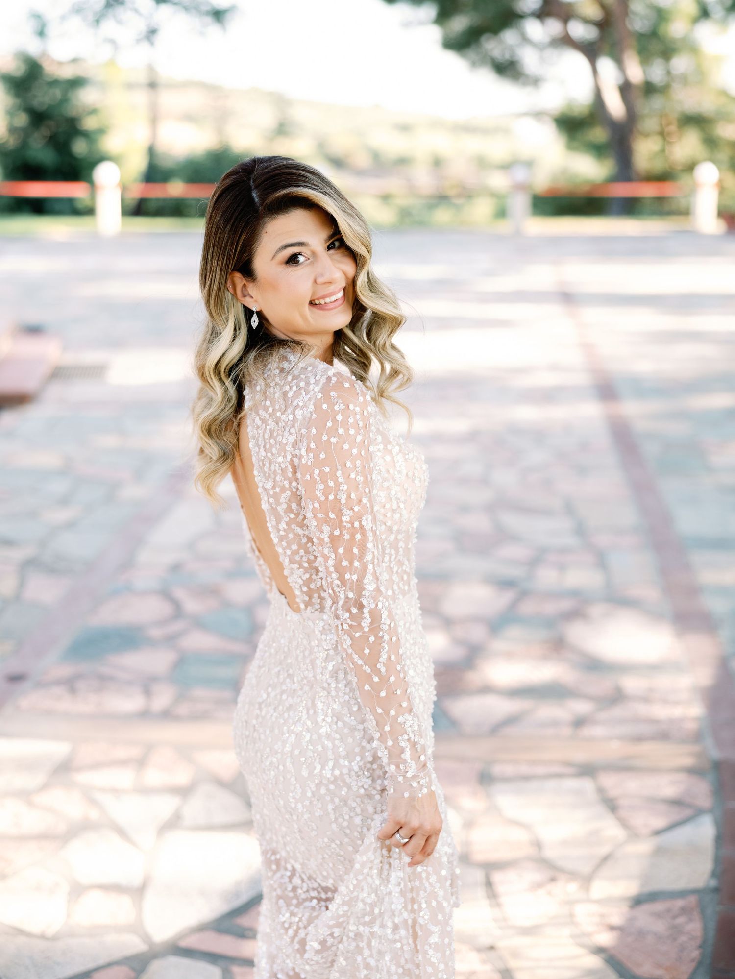 Bride in sparkling lace gown twirls gracefully on stone patio during wedding photoshoot.