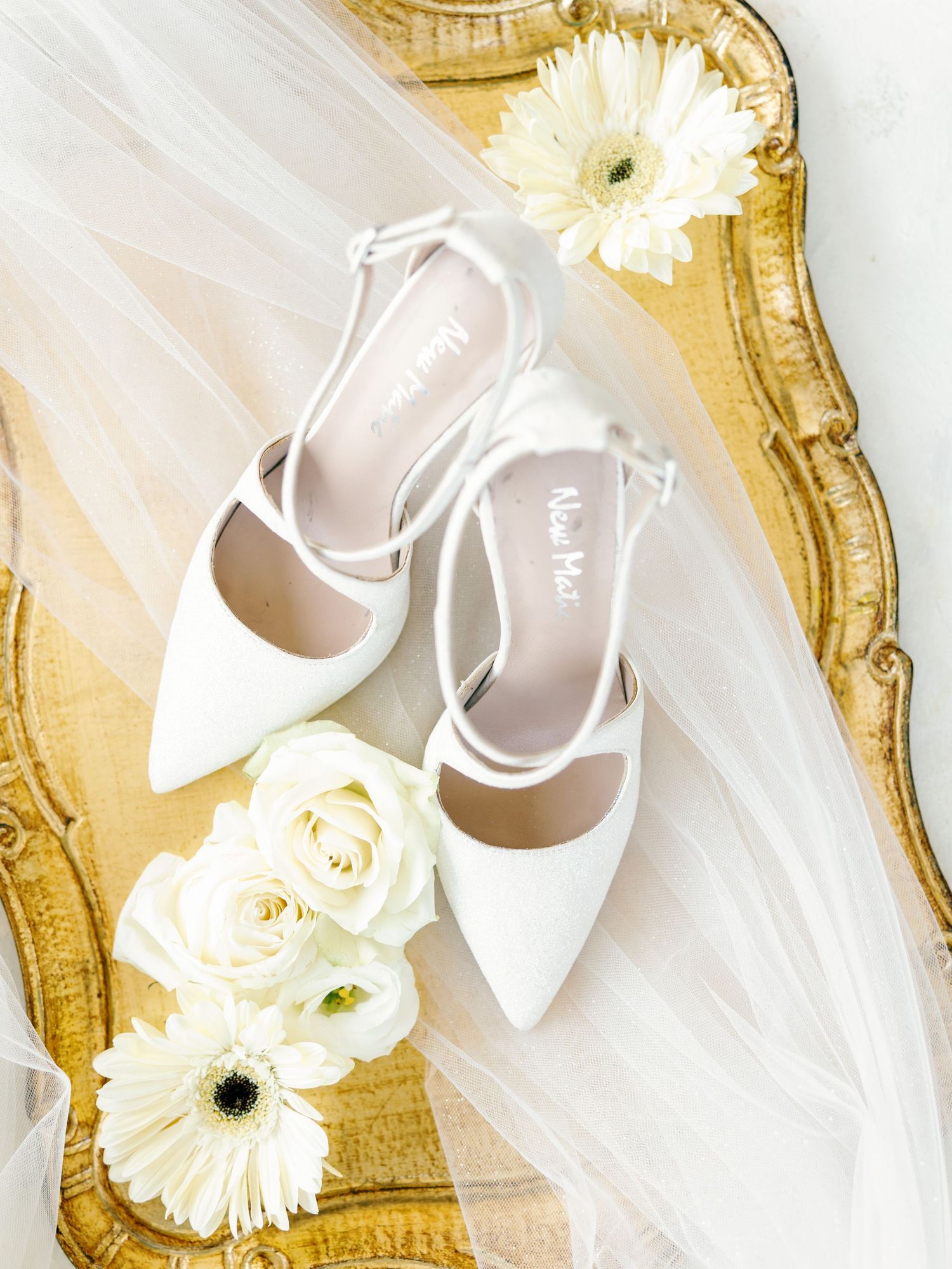 Wedding accessories including white shoes and flowers arranged on ornate gold tray.