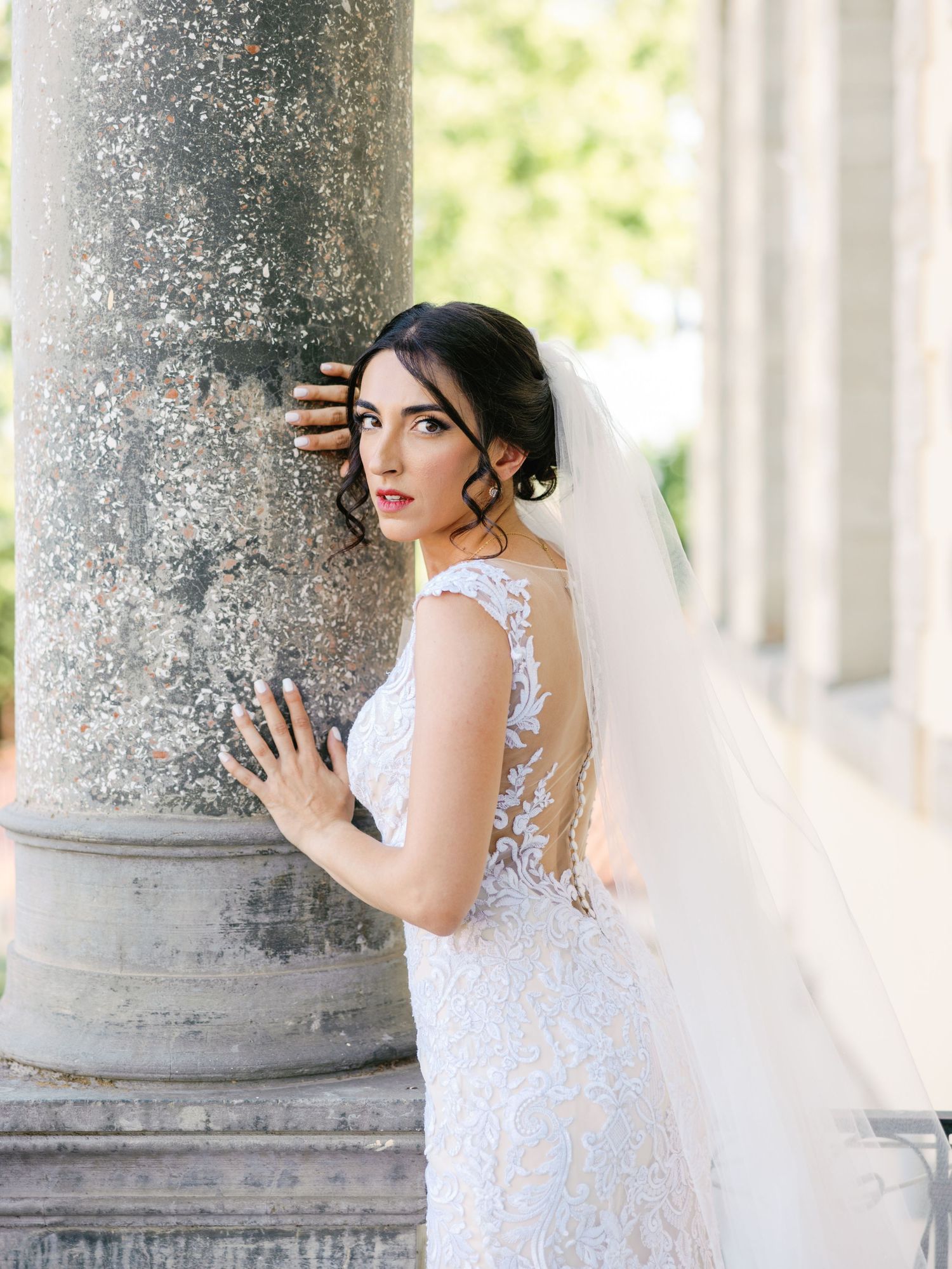 Elegant bridal portrait with bride leaning against classical stone column.