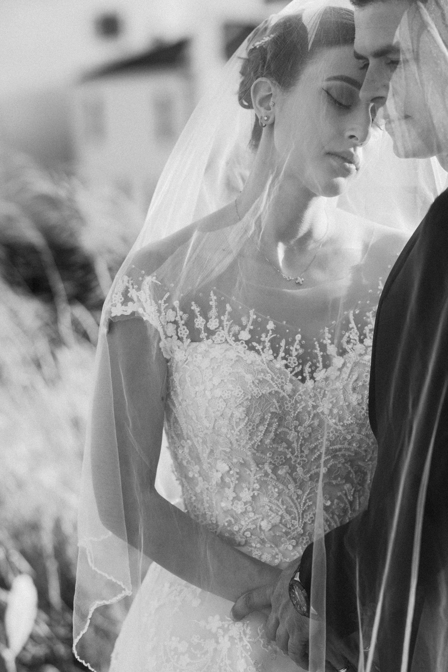 Black and white portrait of bride in detailed lace wedding gown with veil.