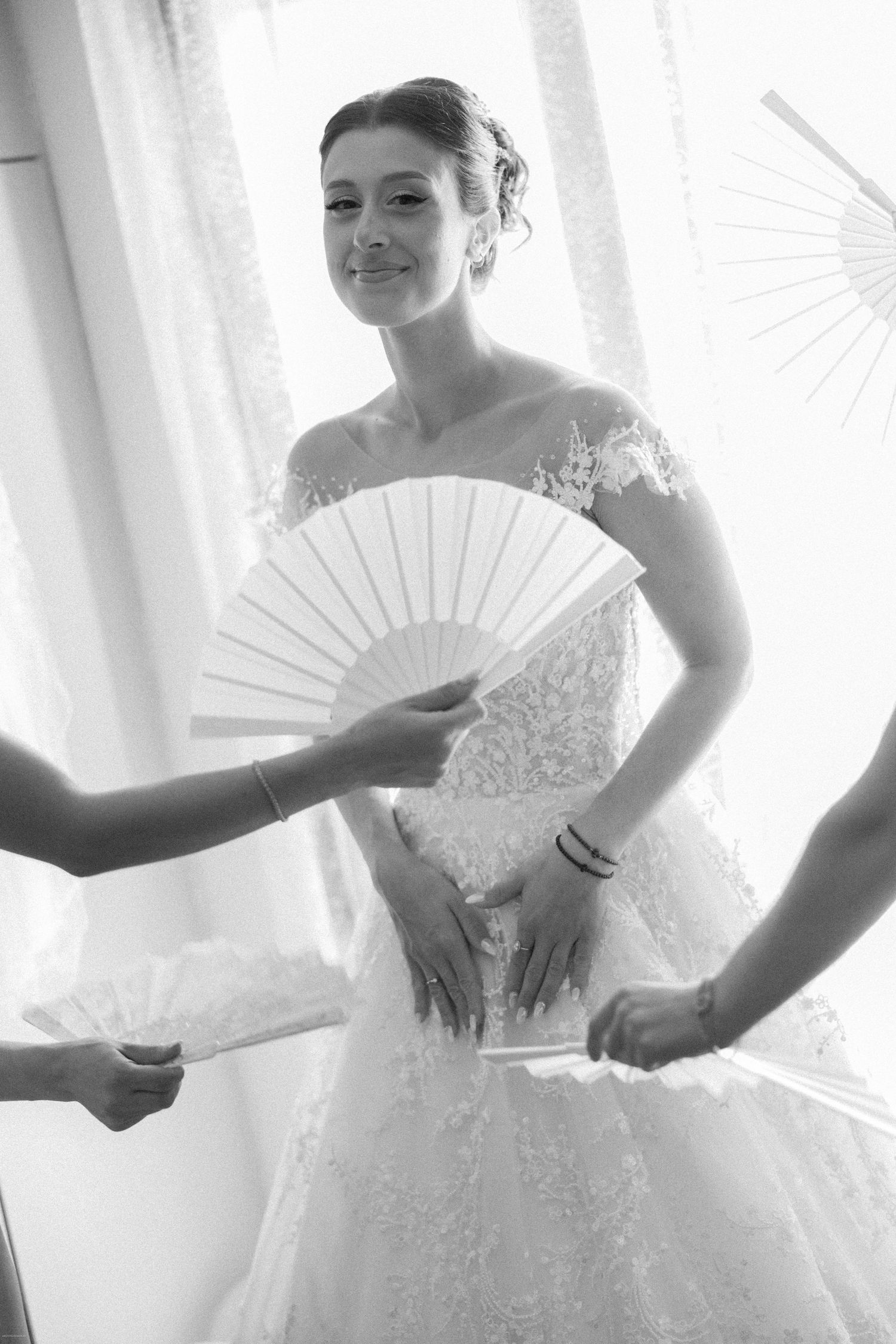 Bride holding white paper fan in elegant lace wedding gown.