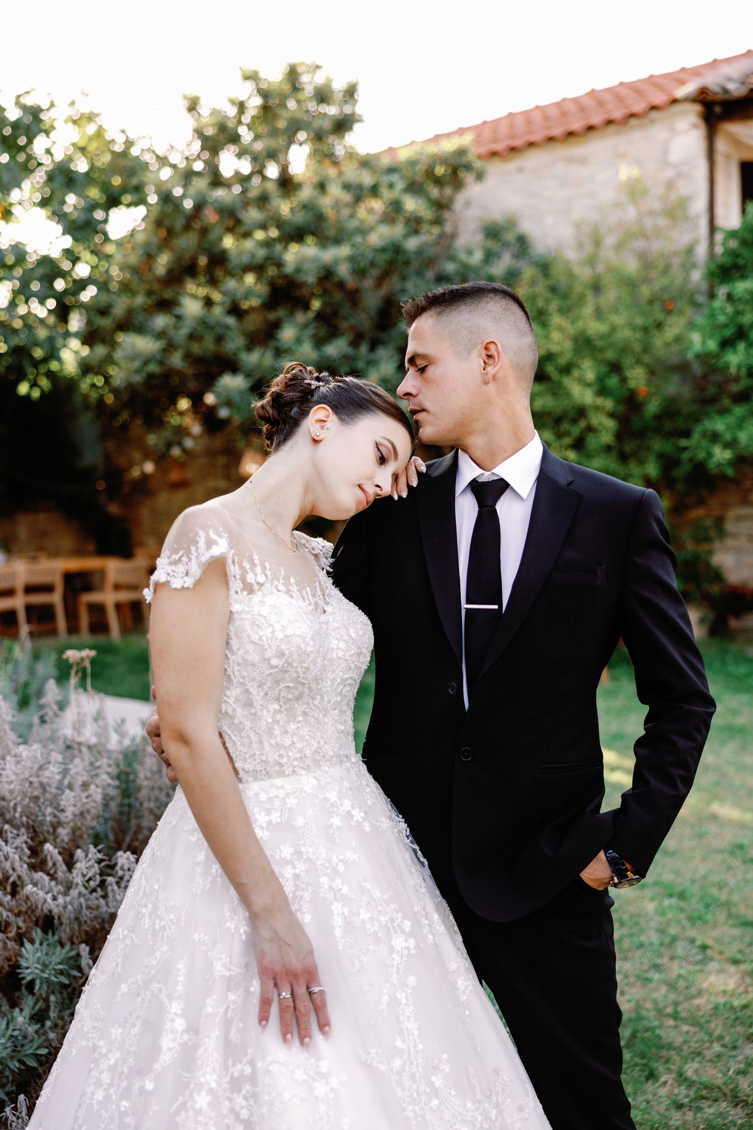 Couple sharing romantic moments in formal wedding attire against garden setting.