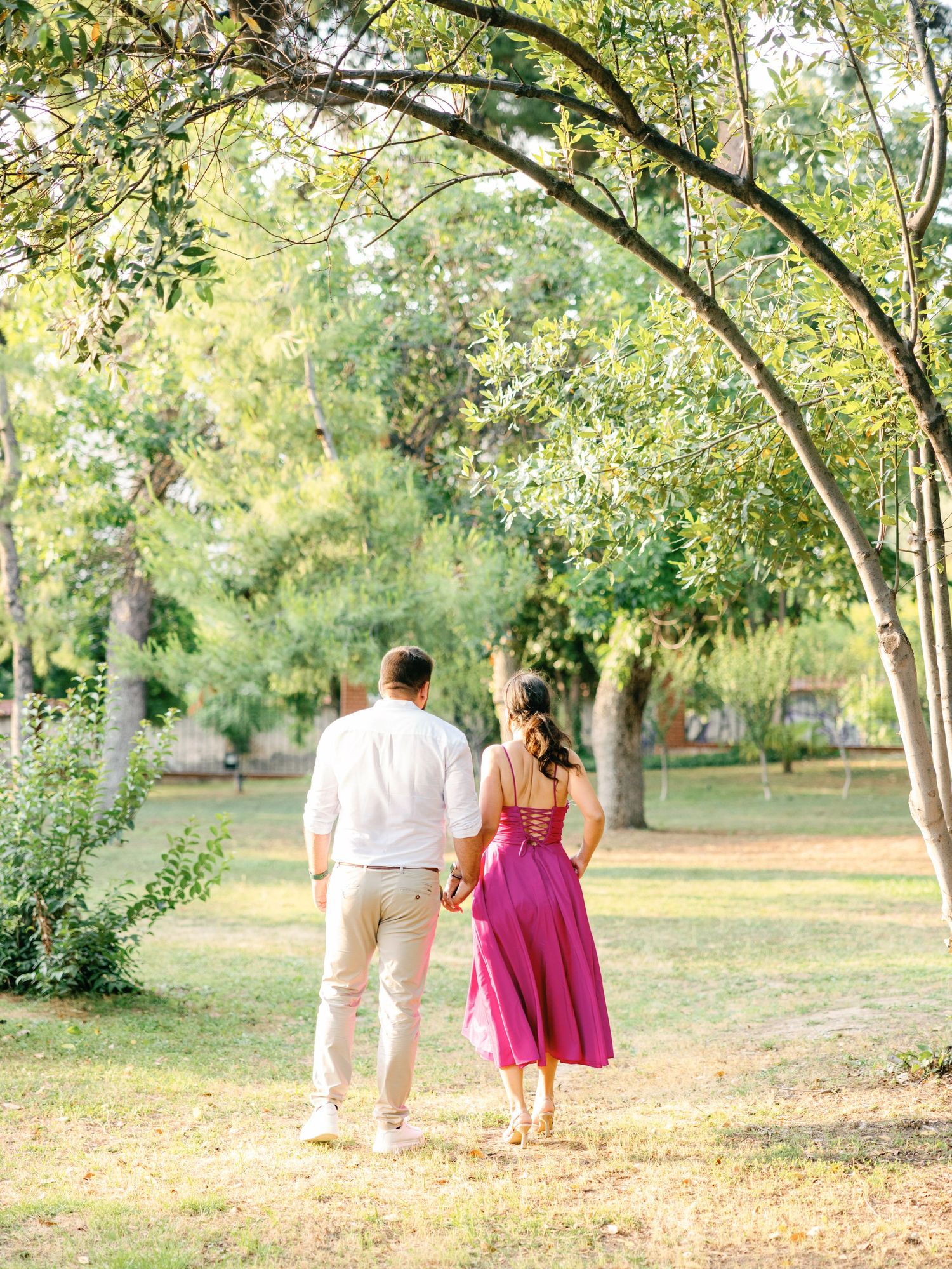 A couple strolls together through a serene garden path lined with trees during golden hour.