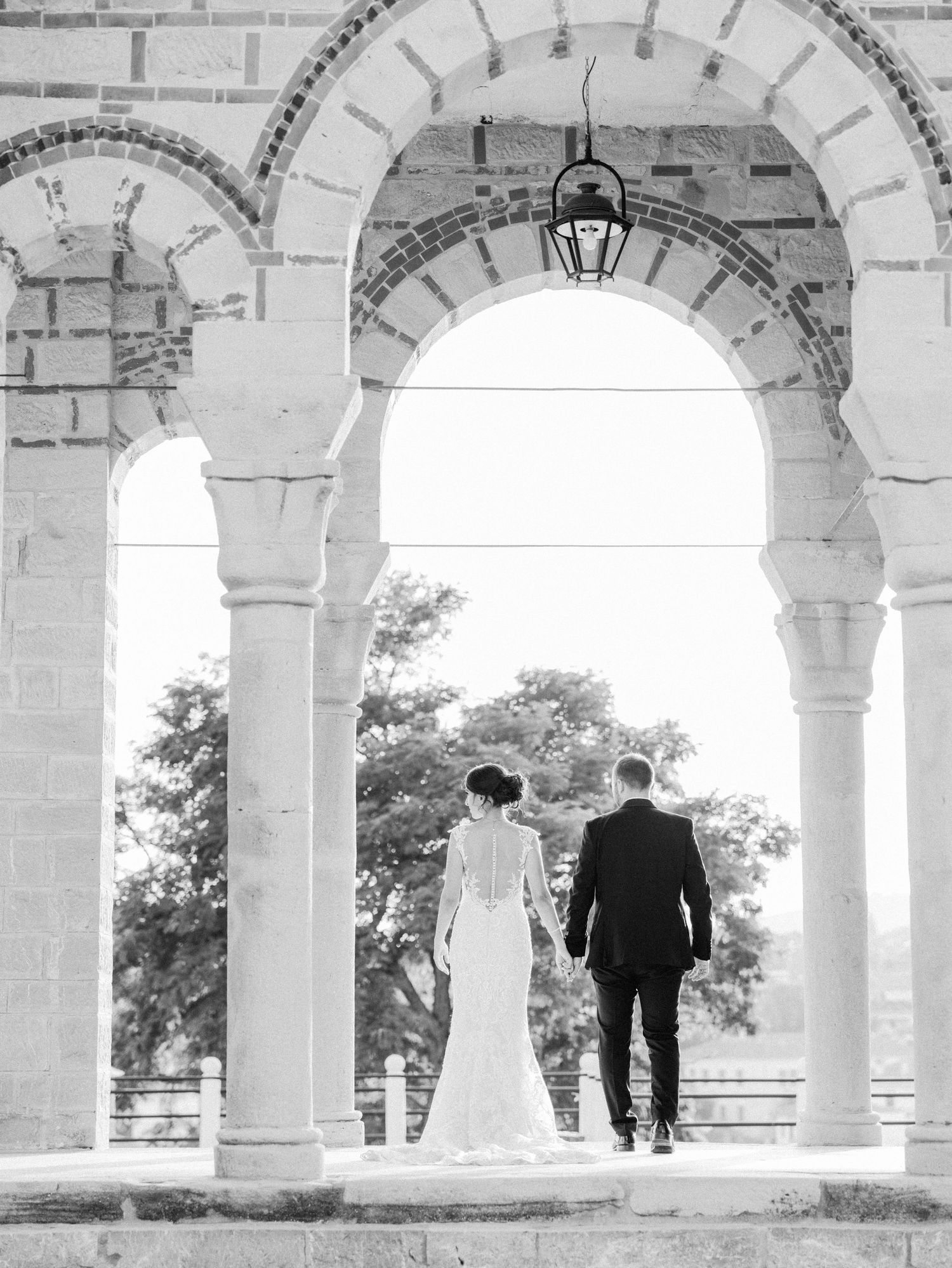 A black and white silhouette of a couple standing beneath grand stone arches.