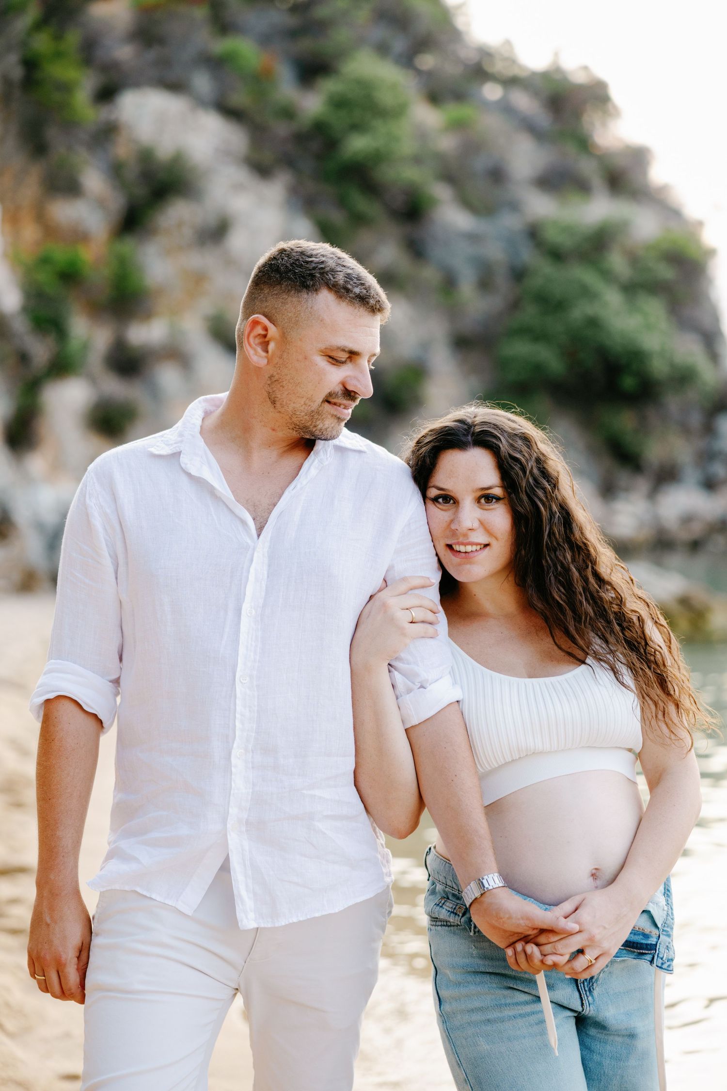 A couple shares intimate moments during a beach photoshoot in matching white outfits.