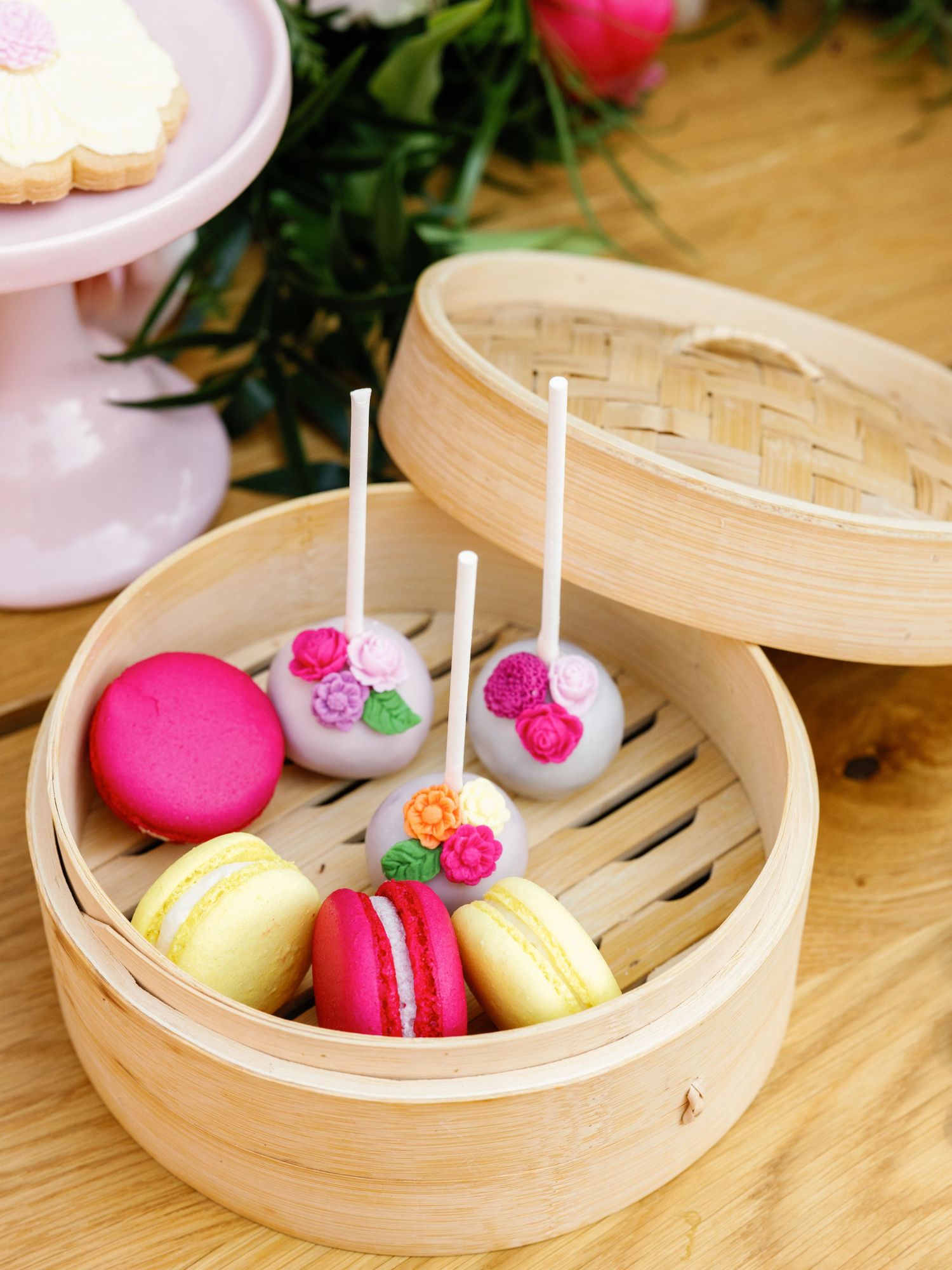 Colorful macarons and lollipops arranged in traditional bamboo dim sum steamer baskets on a wooden surface.