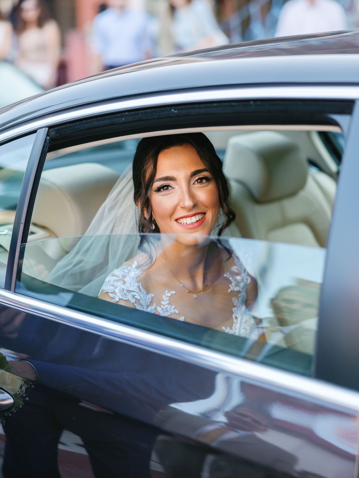 An elegant bride smiles from inside a luxury car on her wedding day.