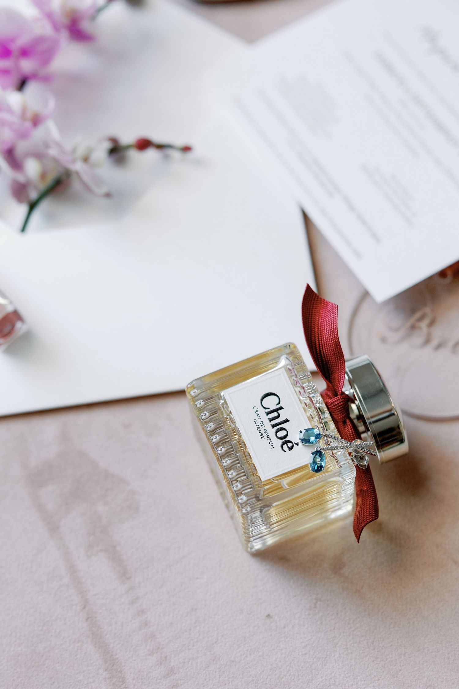 Perfume bottles with red ribbons arranged with cherry blossoms and wedding stationery.