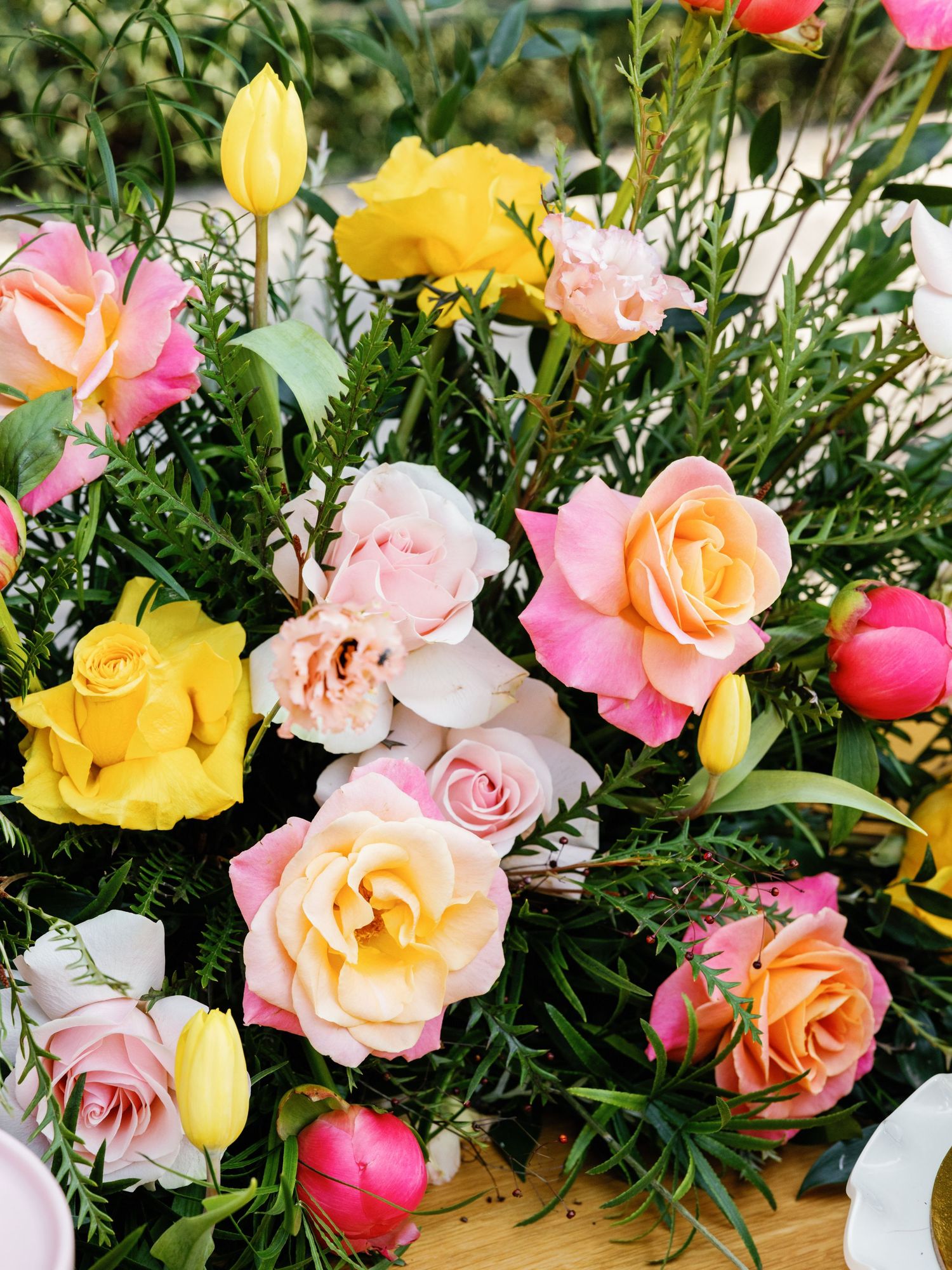 A vibrant floral arrangement featuring pink, yellow, and peach roses with lush greenery in a natural garden setting.