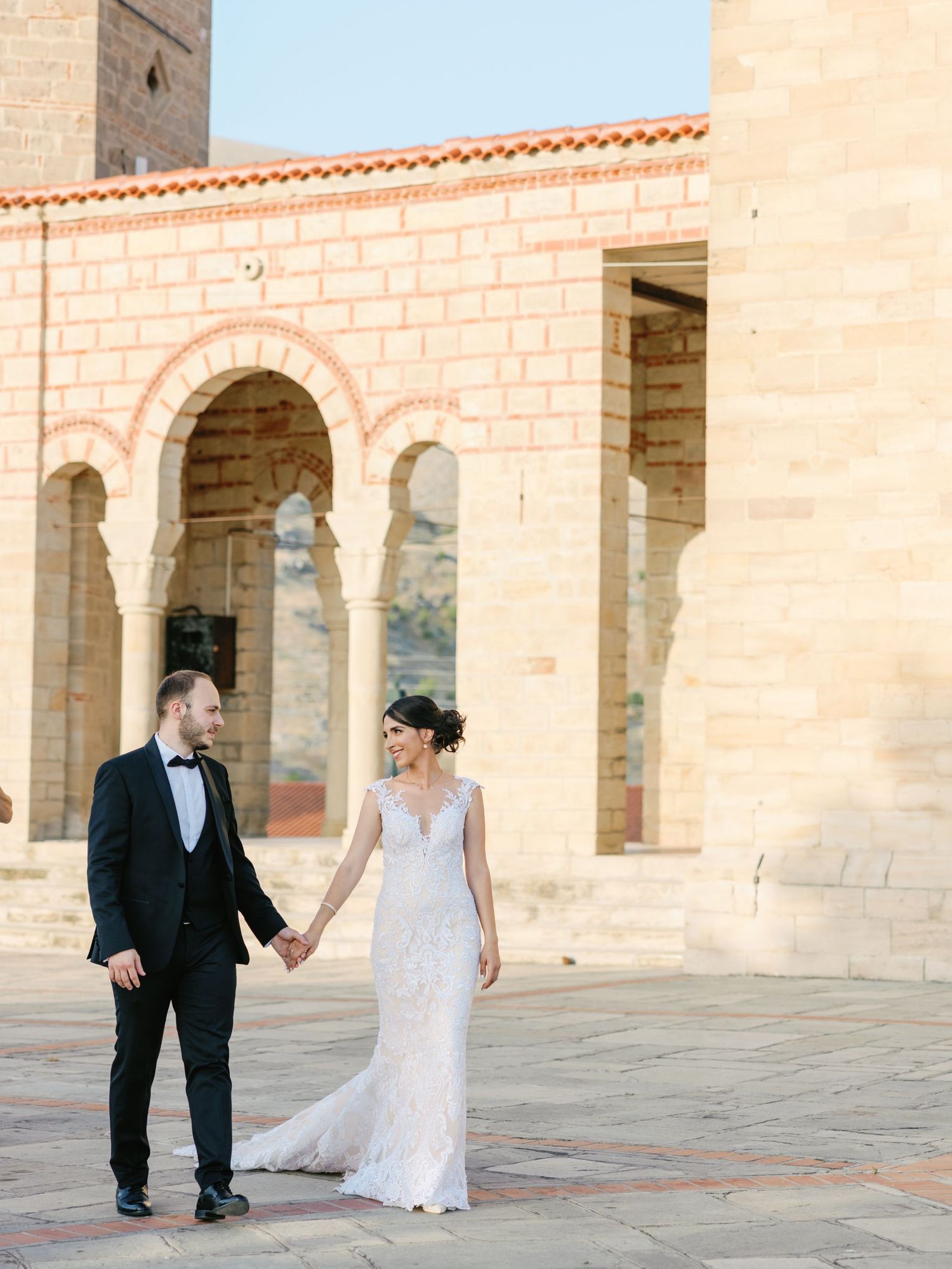 Romantic wedding photos captured in a stone archway colonnade with warm sunlight.