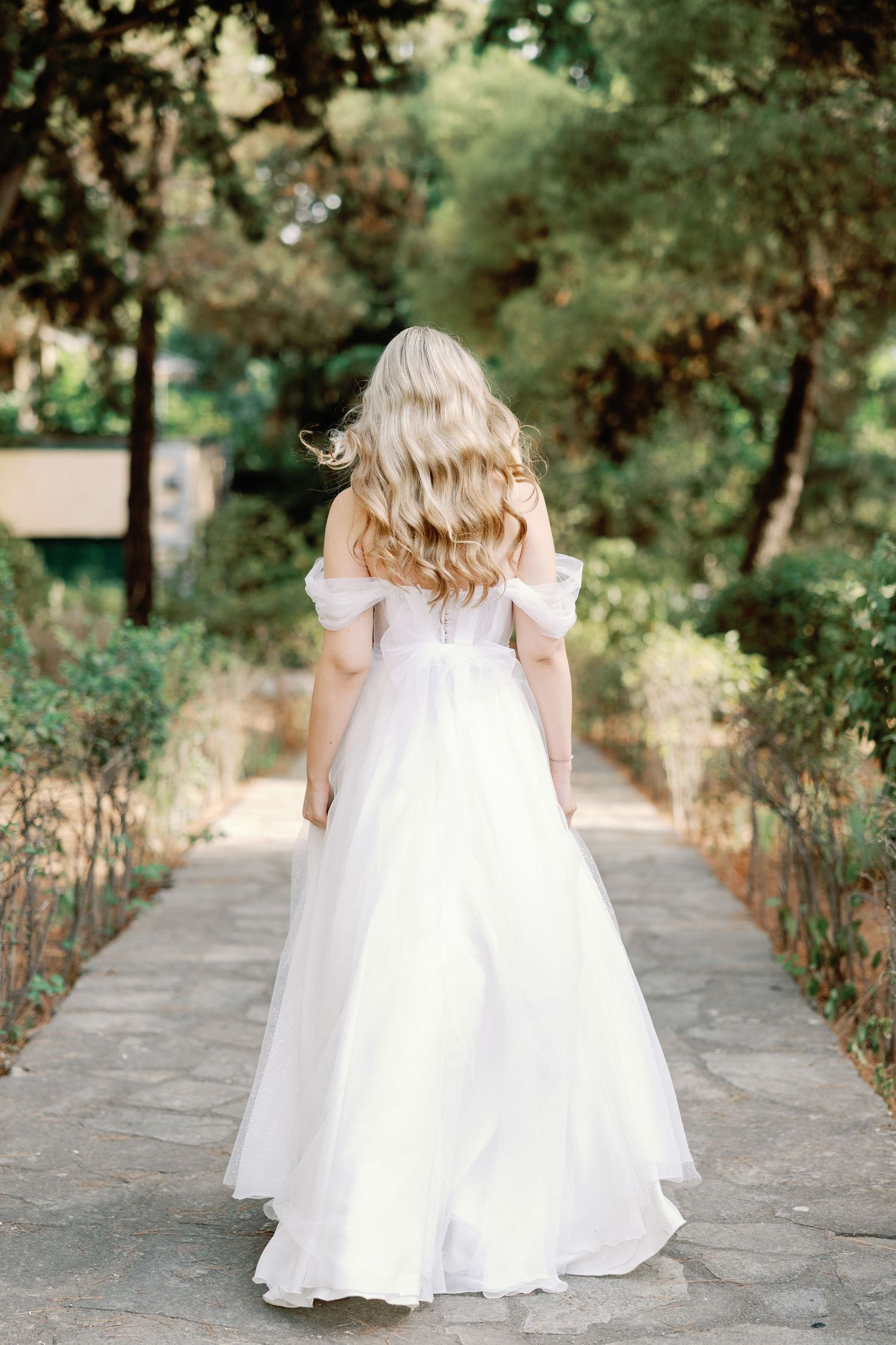 Young flower girls in flowing white dresses walking down a garden path.