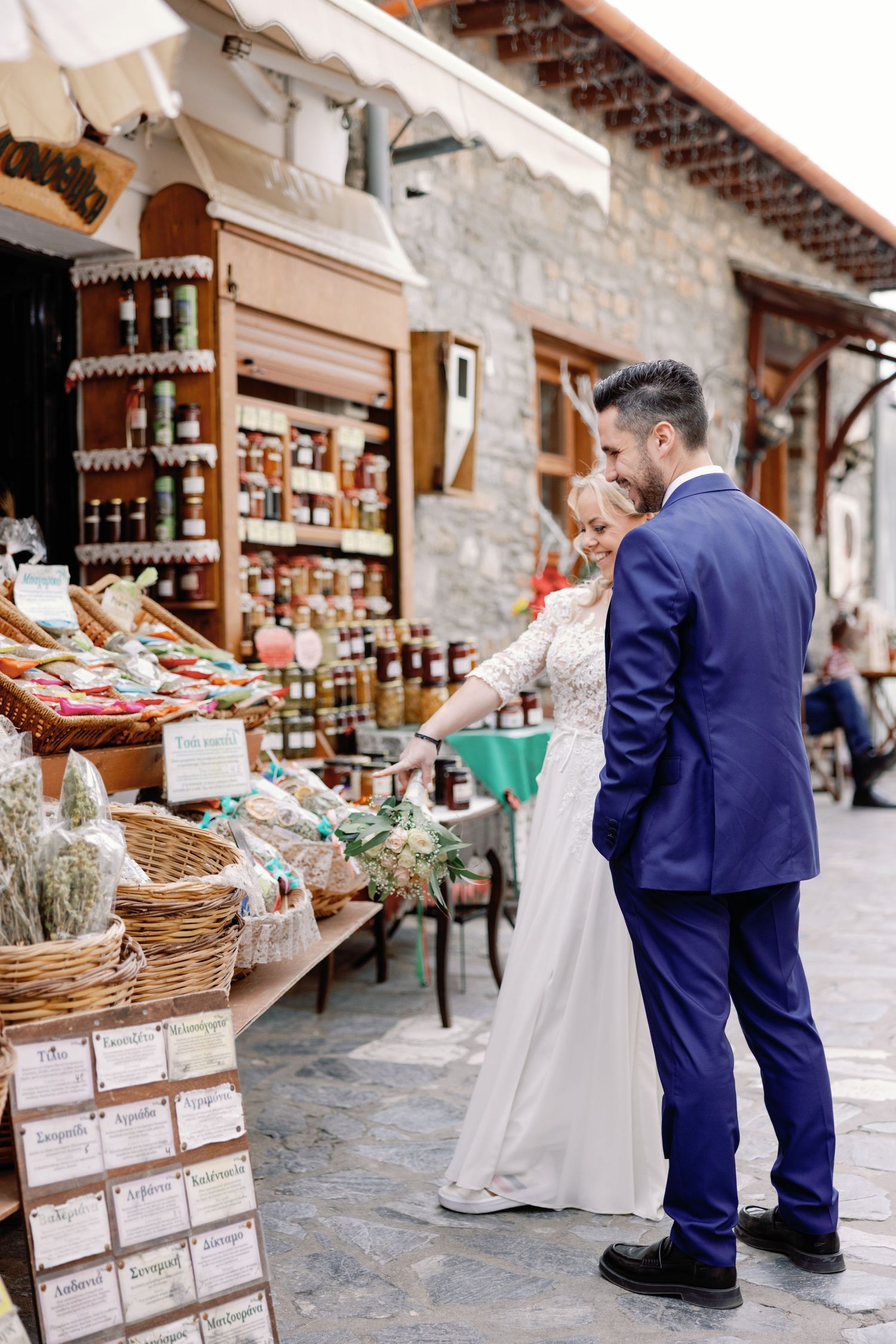 Newlyweds browsing local market stalls with rustic stone walls and baskets.