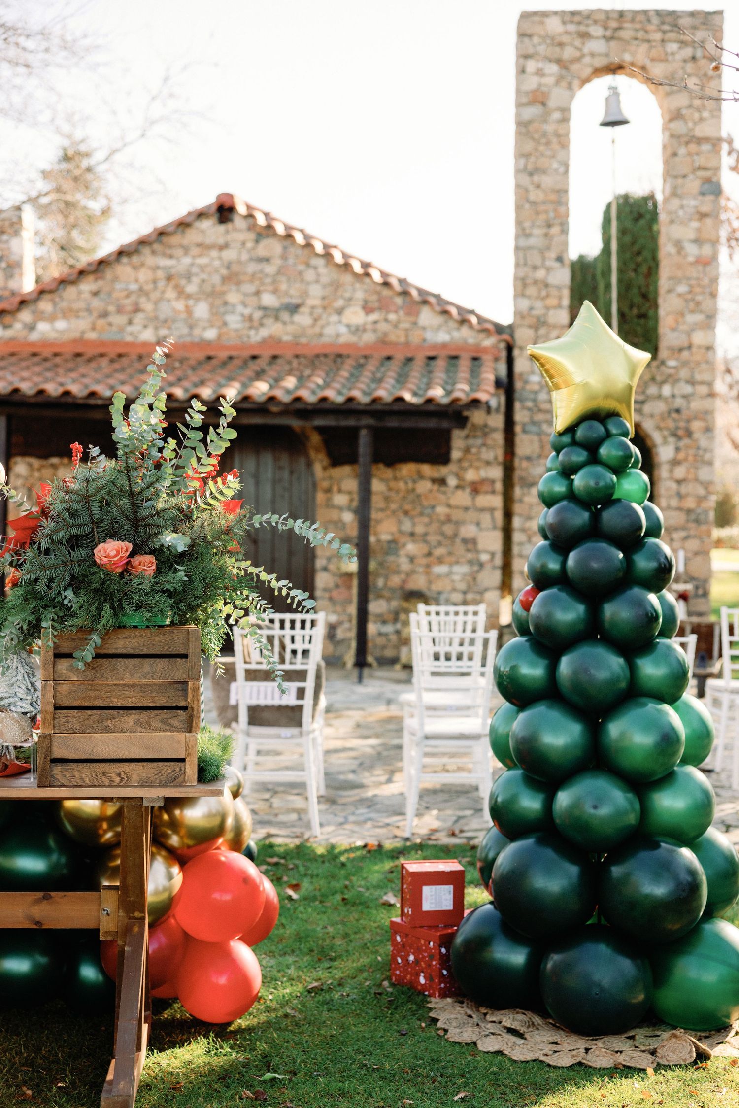 Balloon Christmas tree decorations in dark green with red and gold accents arranged outdoors in a rustic garden setting.