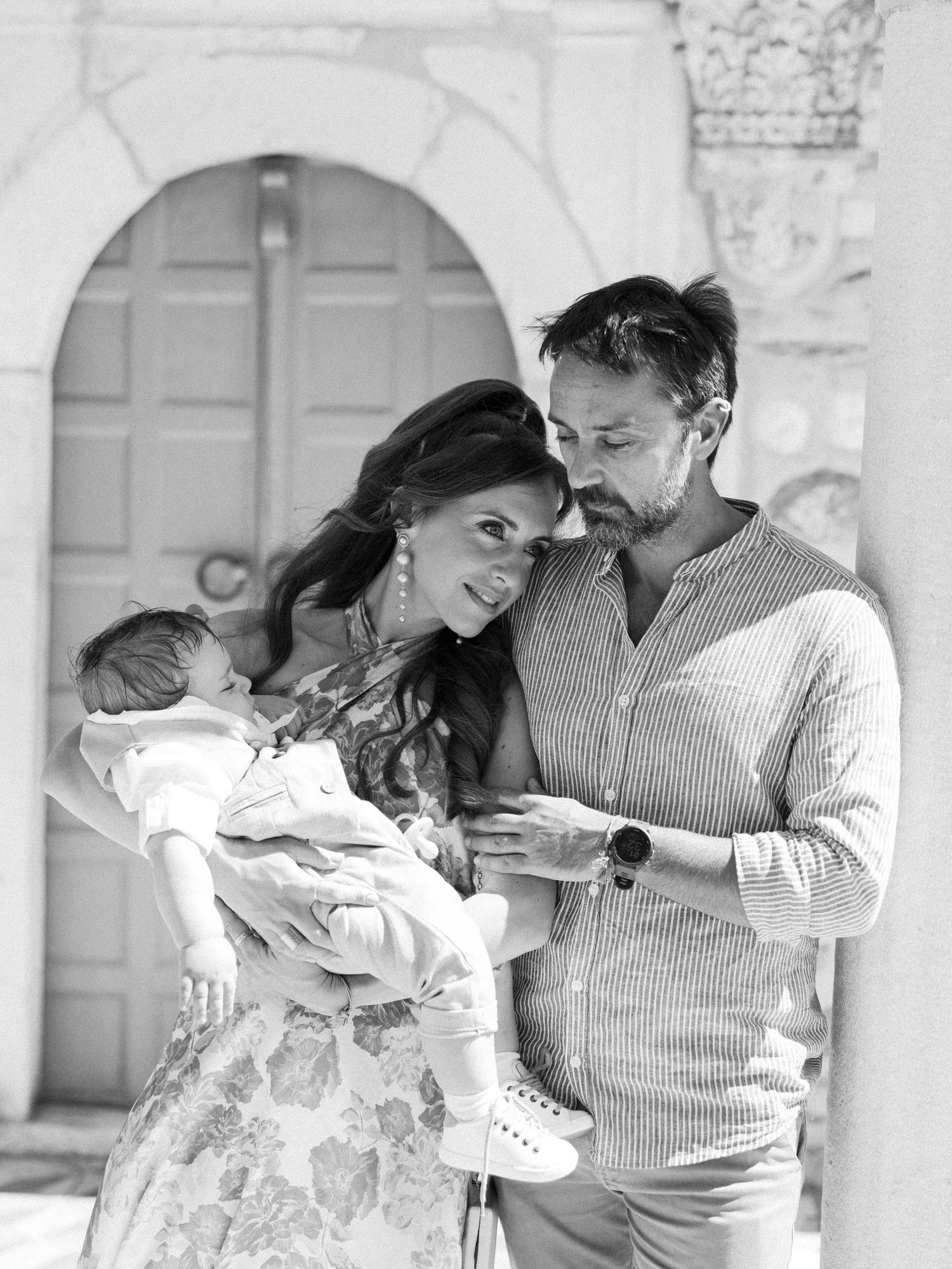 A series of black and white photos showing tender moments between parents and their newborn baby in matching outfits.