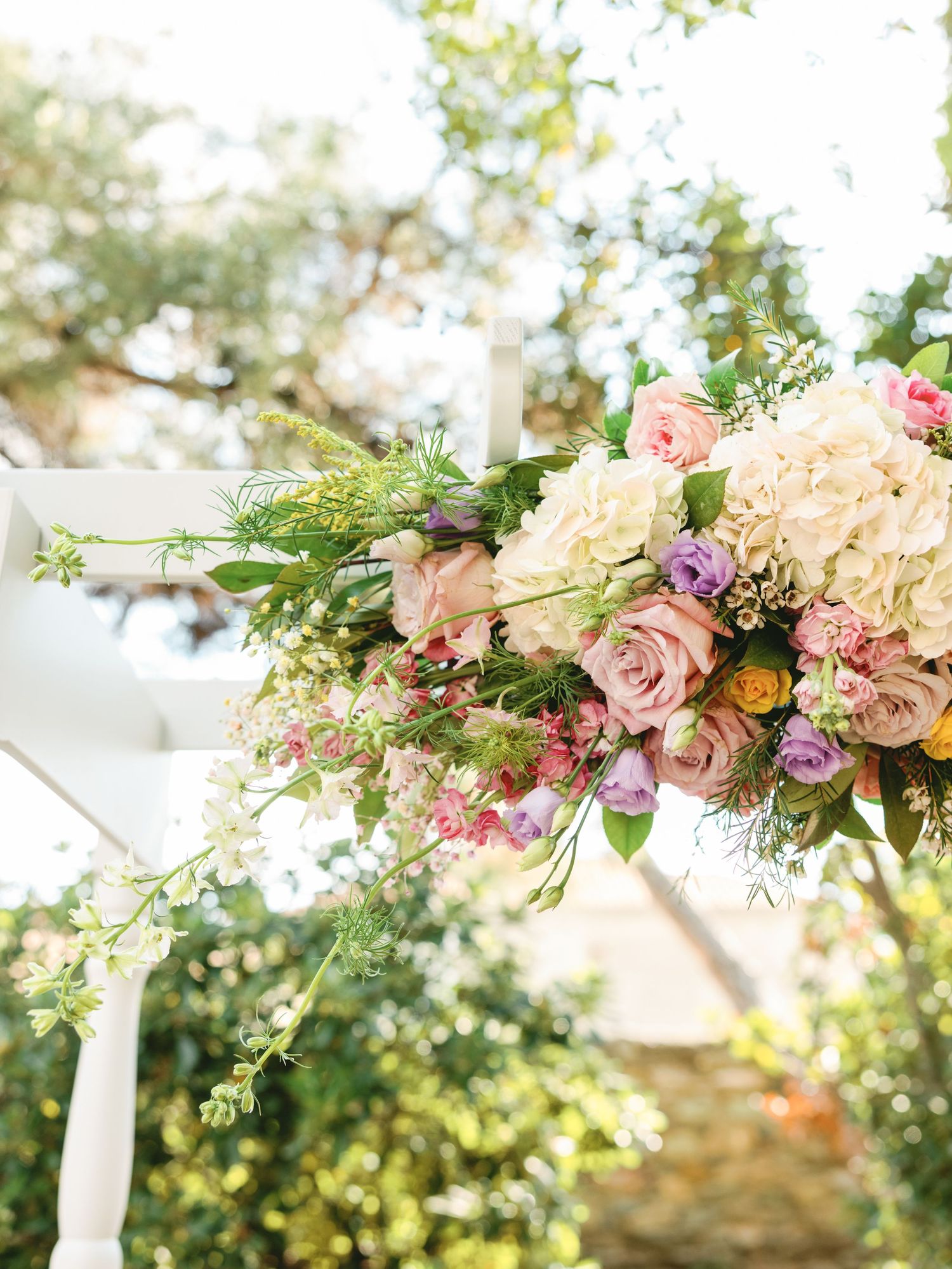 Elegant floral wedding arch decoration with pink roses, hydrangeas and greenery draped with white fabric outdoors.
