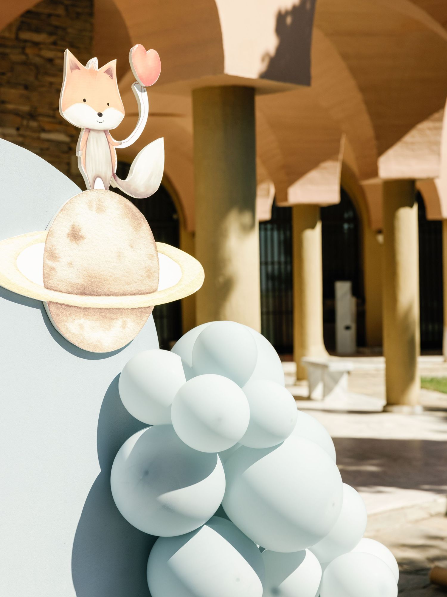 Whimsical light blue balloon sculptures with animal-like forms displayed in an outdoor colonnade space.