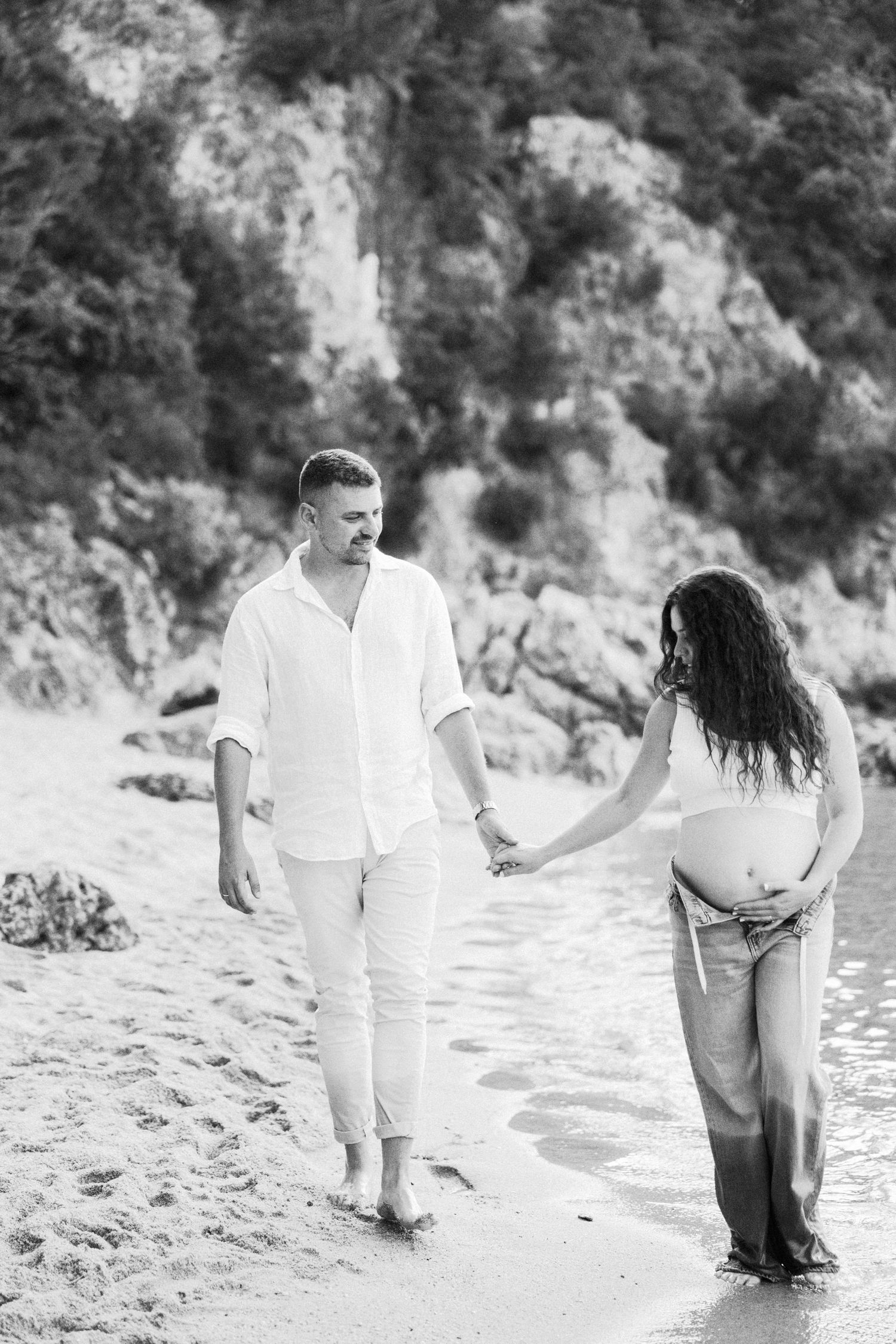 A couple walks and dances together on a sandy beach near rocky cliffs.