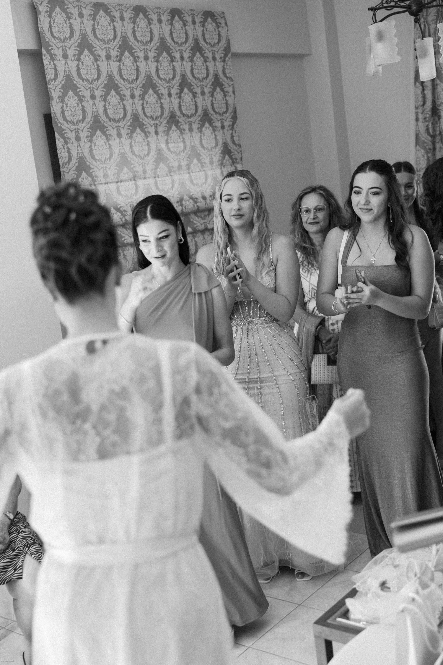 Wedding dress reveal moment with bridesmaids reacting in a room with patterned wallpaper.