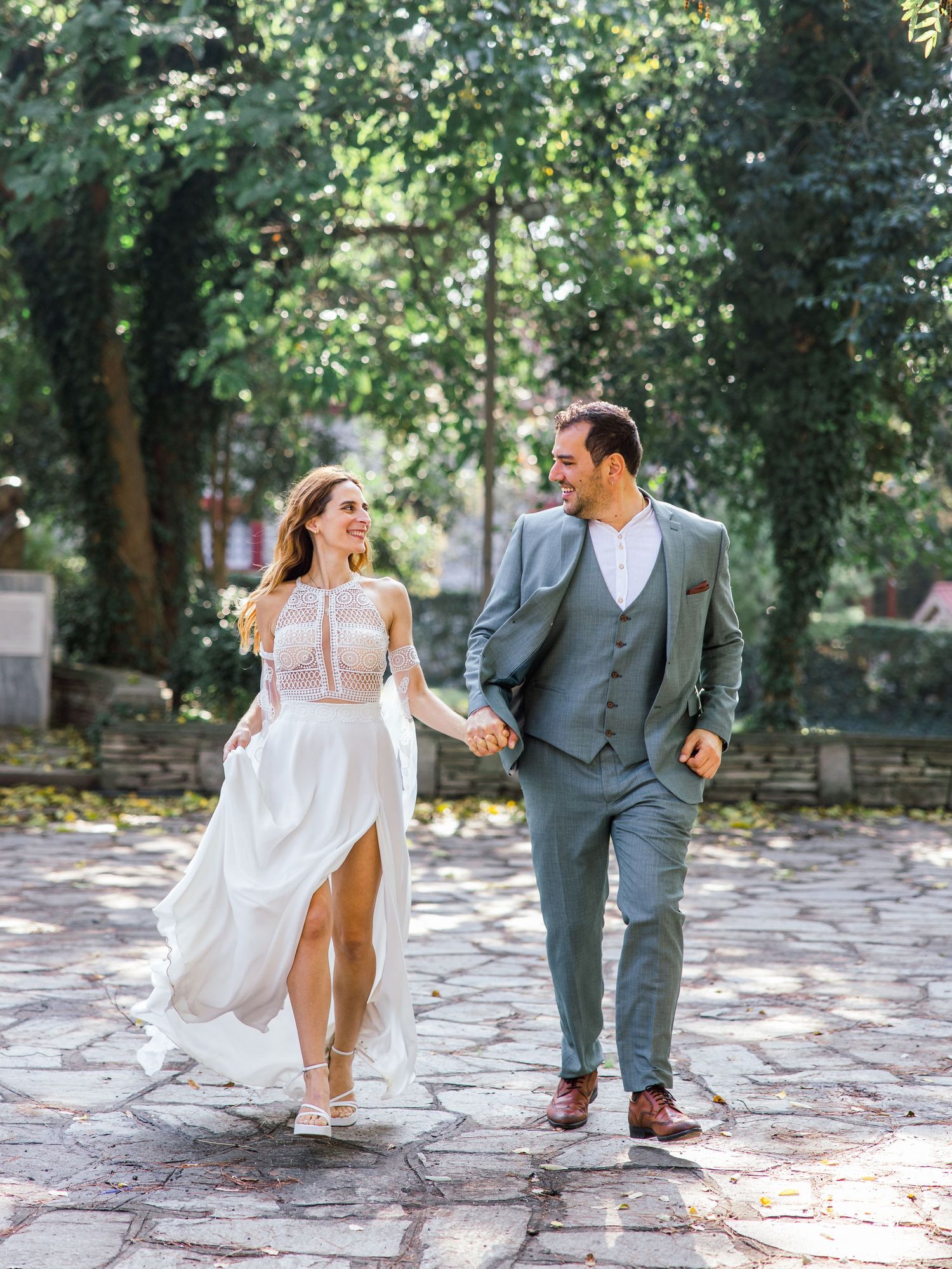 Couple playfully walking and dancing on stone pathway surrounded by greenery.