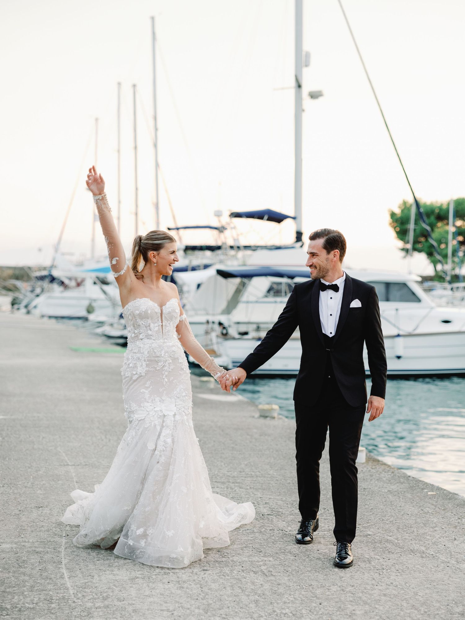 A joyful wedding couple strolling along a harbor with luxury yachts in the background.