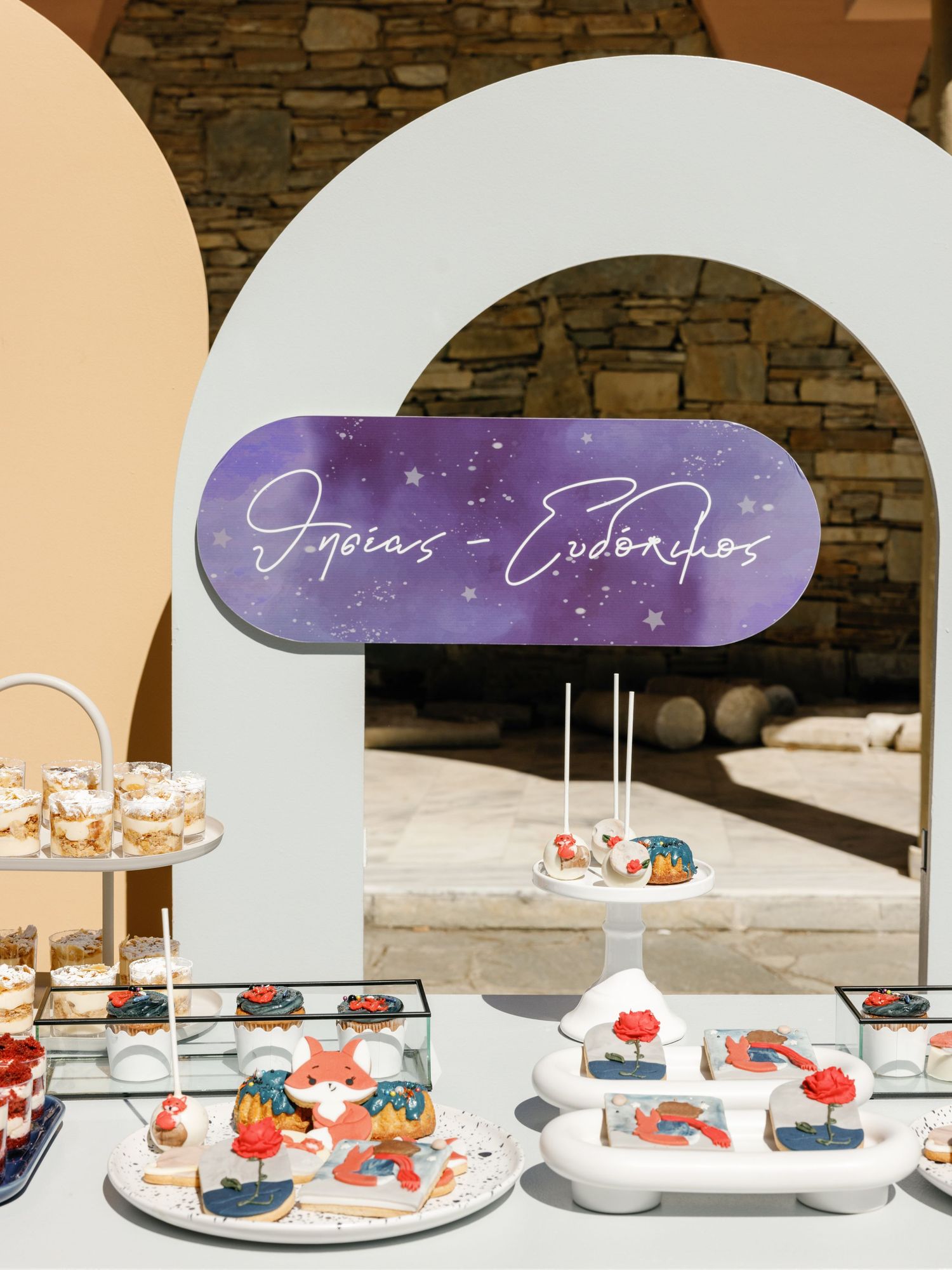 Elegant dessert display with tiered white cake stands holding colorful pastries under arched stone architecture.