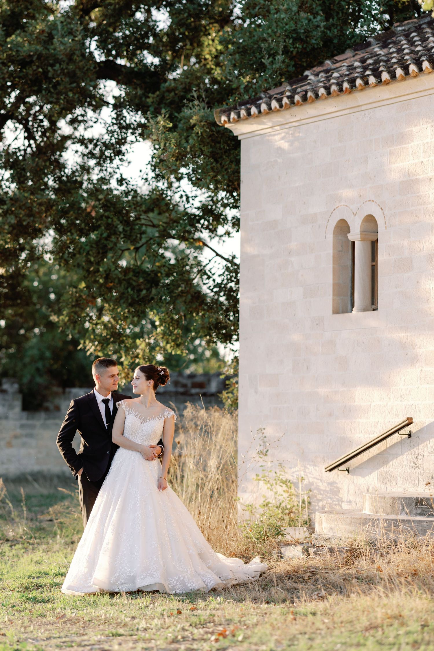Wedding couple posing romantically outside Mediterranean-style building with arched windows.