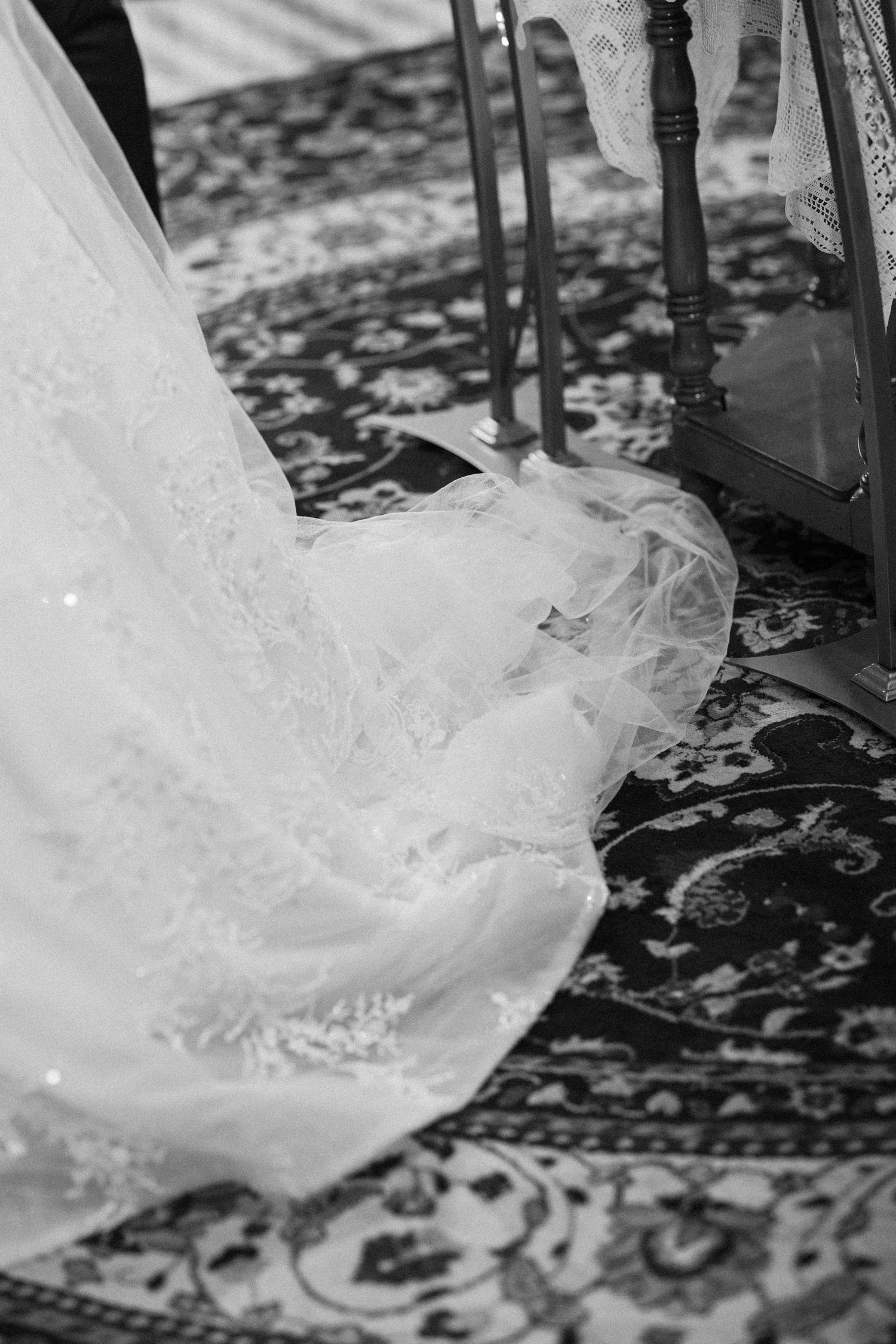 Close-up details of delicate white lace and tulle from a wedding dress trailing on a patterned floor.