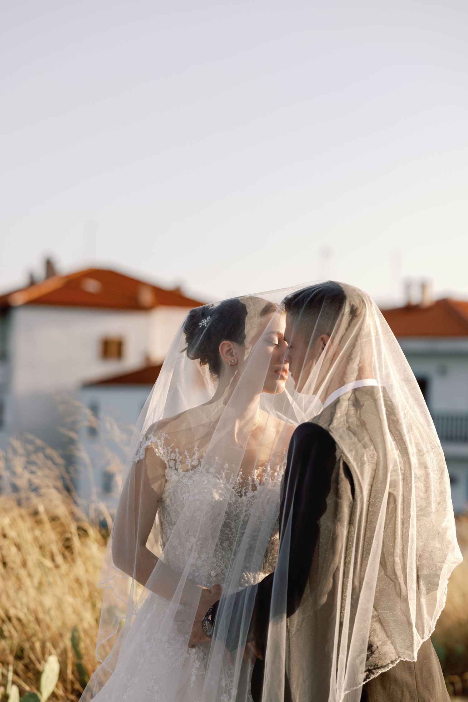 Silhouetted wedding couple embraces against bright sky during sunset.