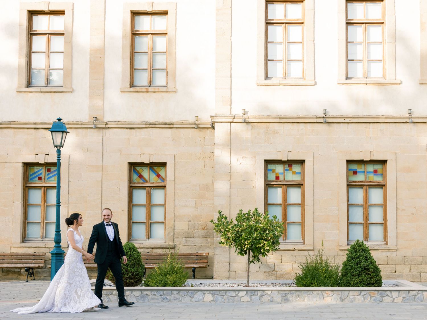 Wedding couple walking together along exterior stone wall with turquoise window frames.