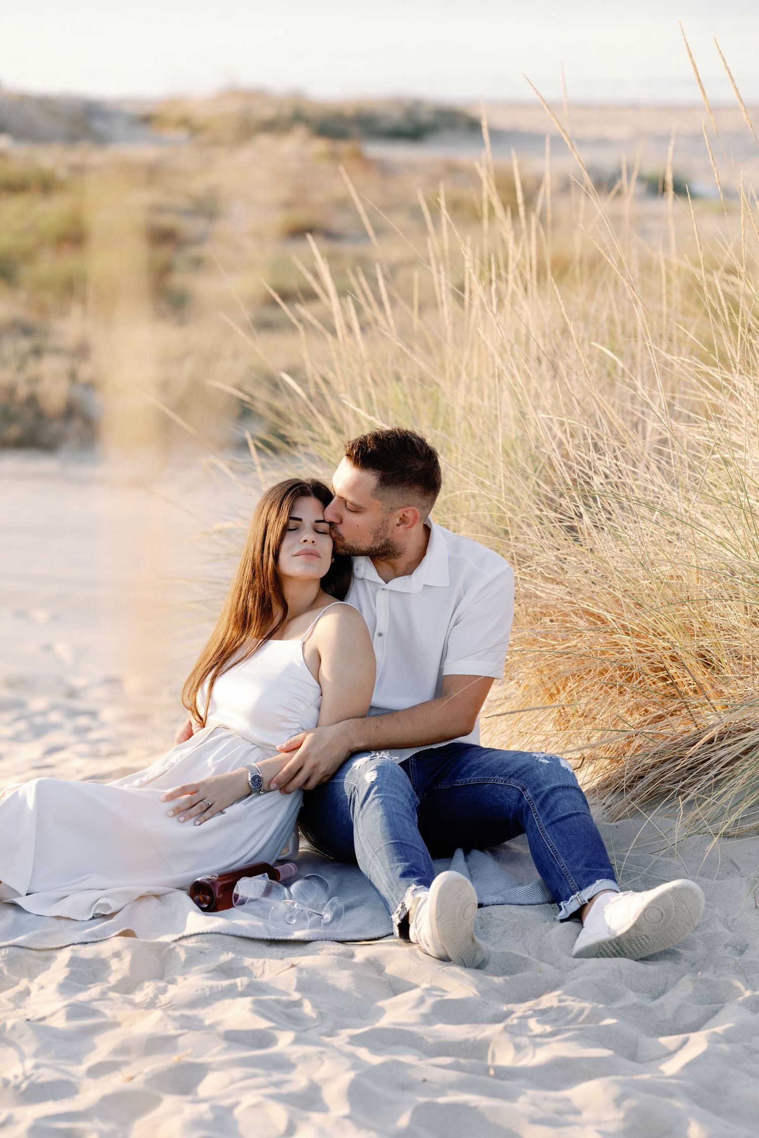 Romantic couple lounges together on sandy beach dunes during golden hour.