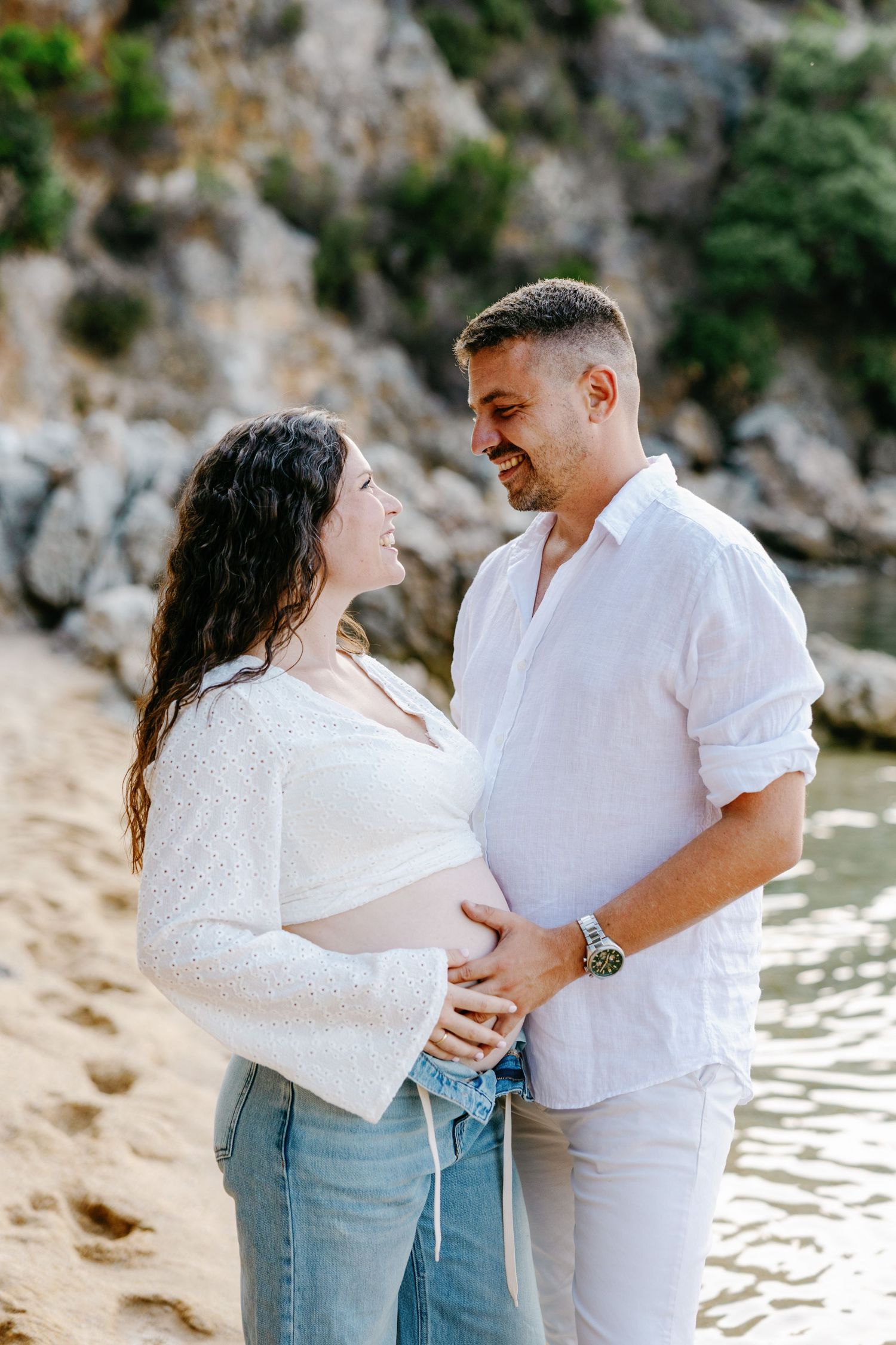 Couple sharing intimate moments on a rocky beach during sunset photoshoot.