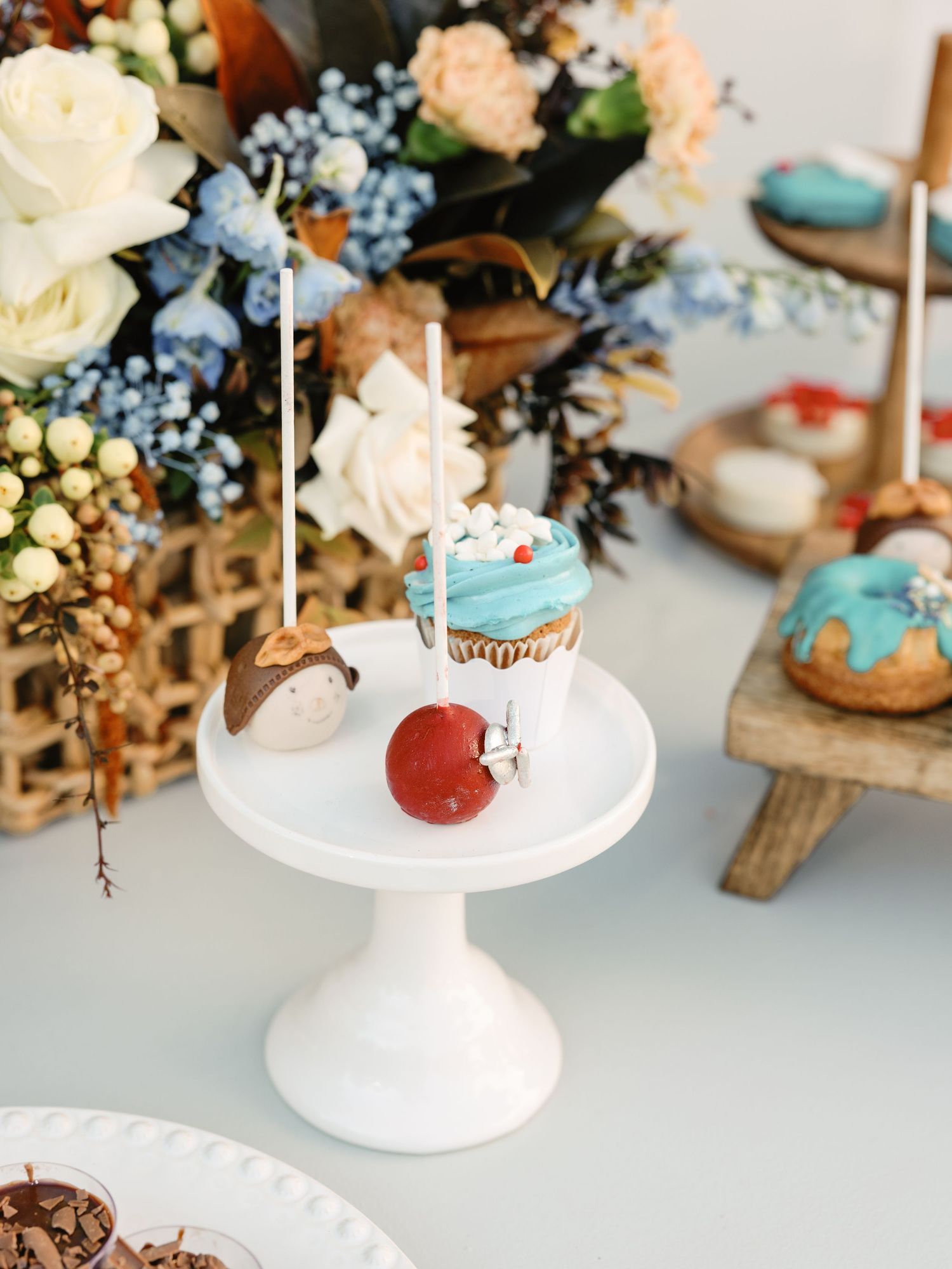 White cake stands display elegant desserts and treats with delicate floral arrangements on a rustic wooden table setting.