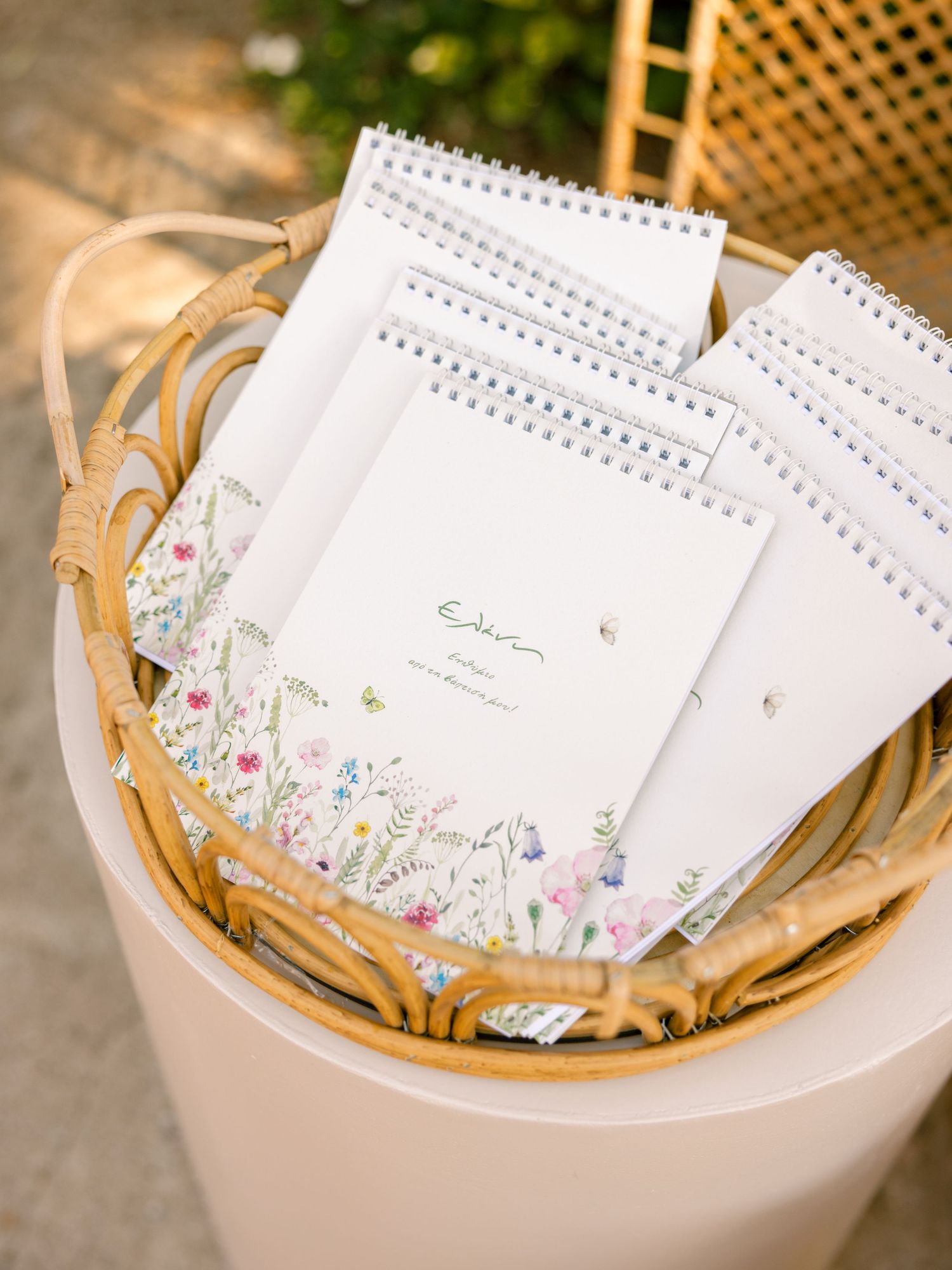 A collection of white spiral-bound notepads with delicate floral designs arranged in woven baskets.