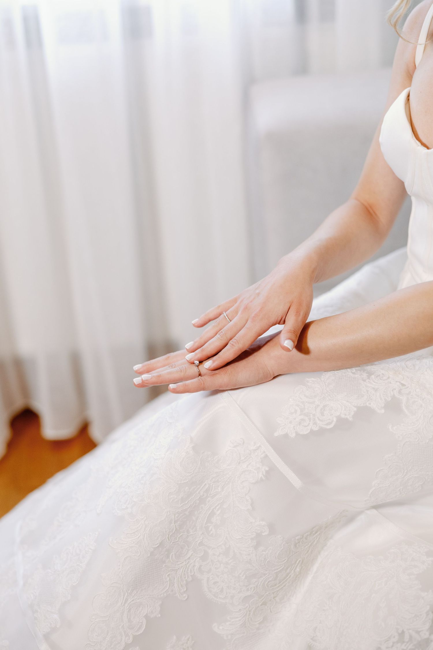 Close-up of hands smoothing out delicate white lace on a wedding dress.