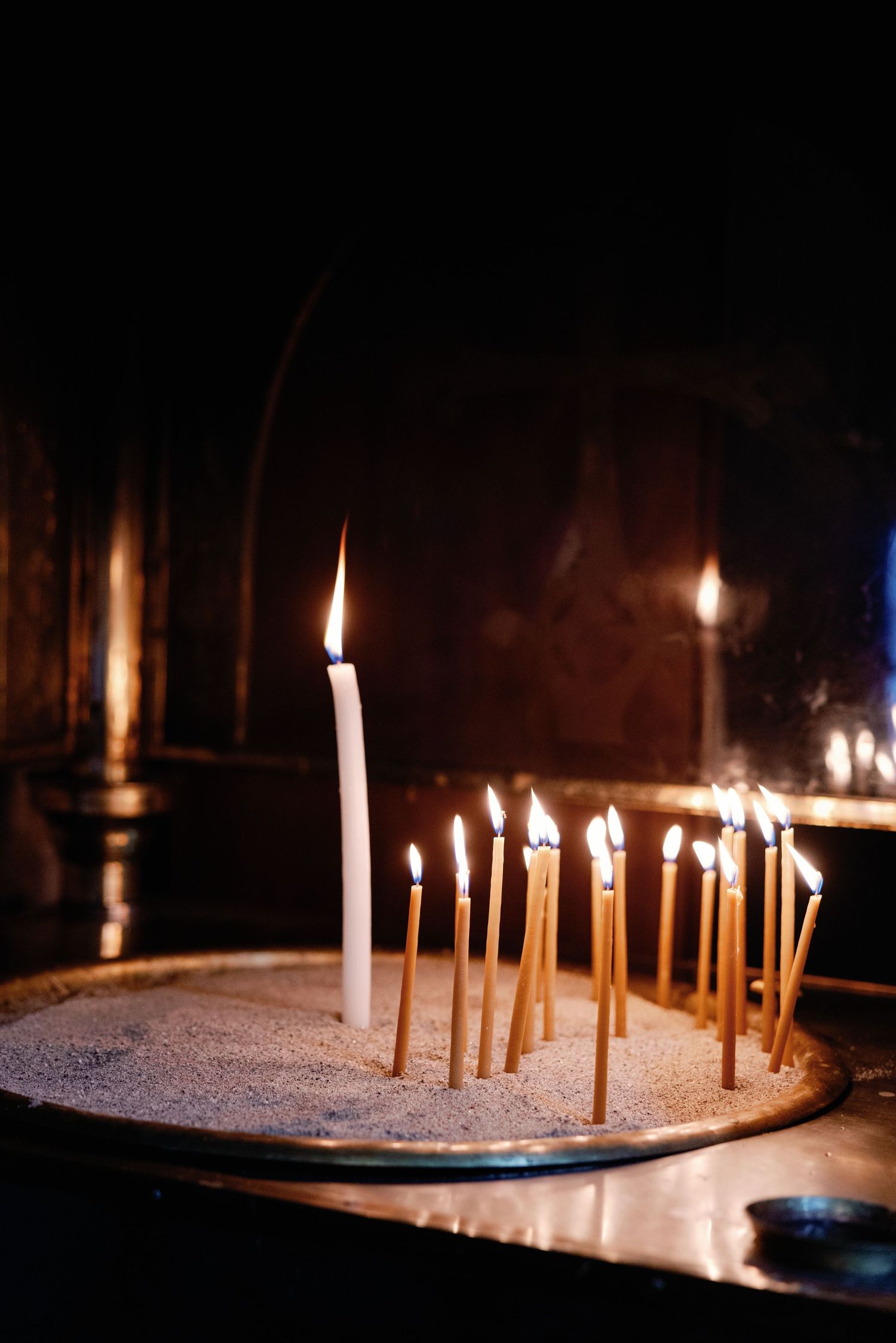 Lit candles glowing in the dark on a traditional church candleholder.