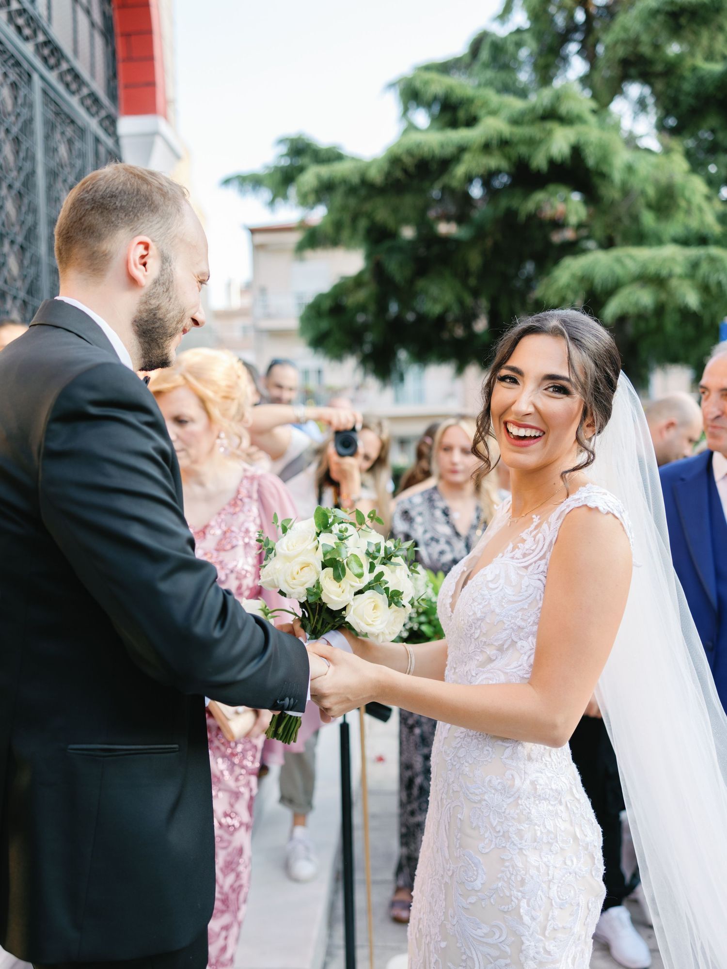 A joyful outdoor wedding celebration with guests and couple sharing laughter outside a stone building.